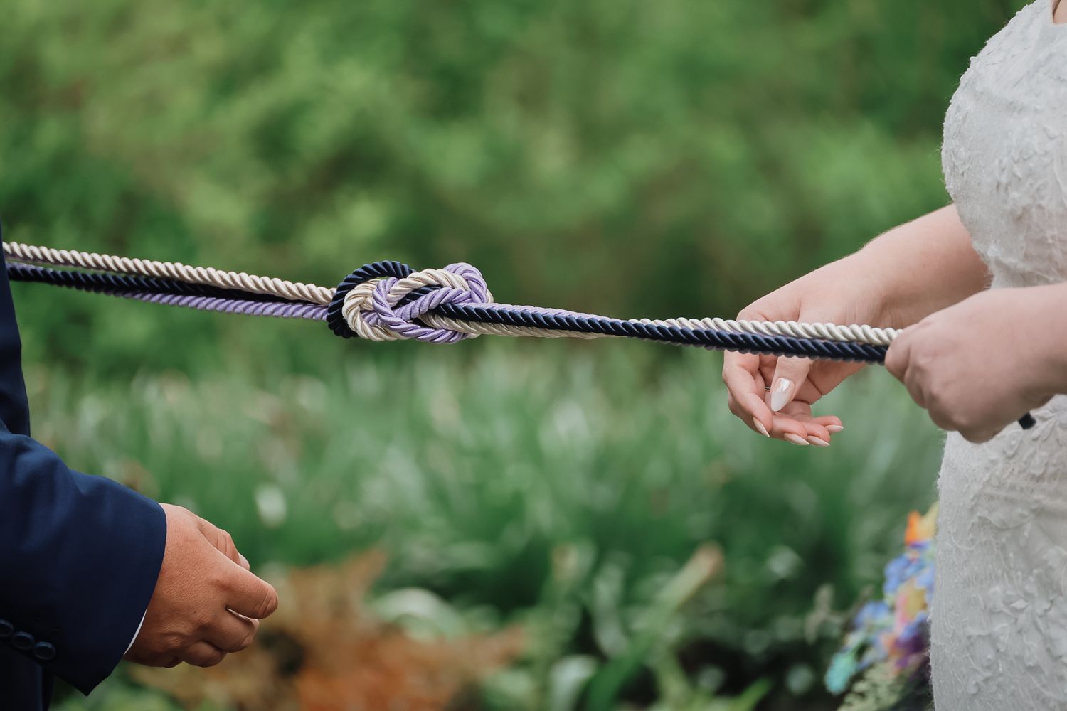 Bride and groom tying a nautical knot ceremony rope during an outdoor wedding celebration.