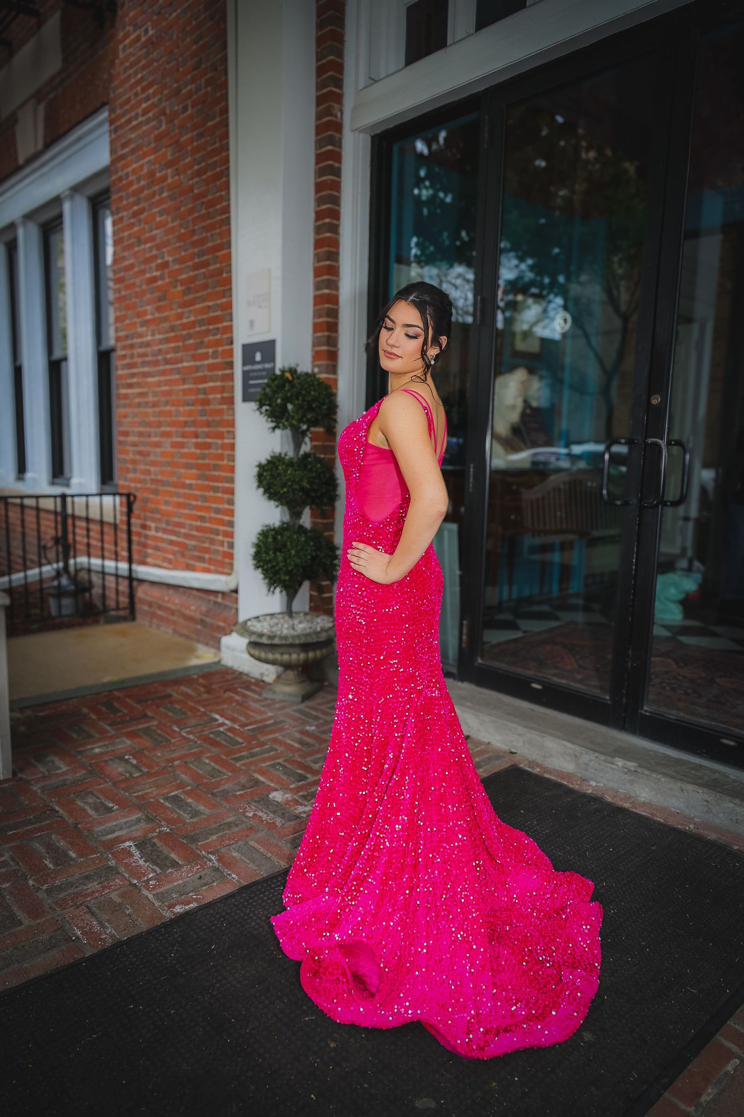 Woman in a stunning hot pink sequined mermaid gown with train poses outside a brick building.