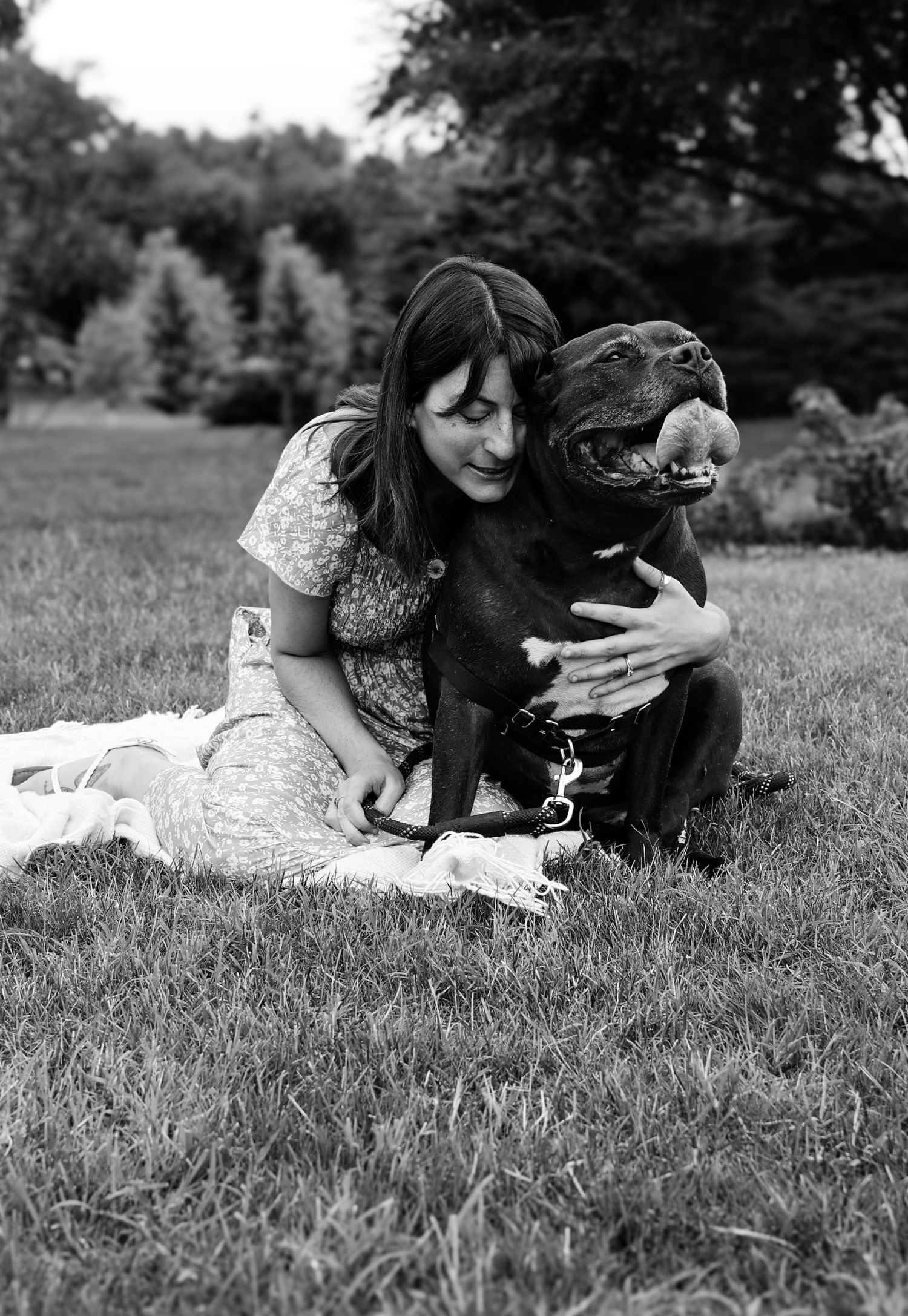 A person and black dog share a tender moment lying together on grass in black and white photography.