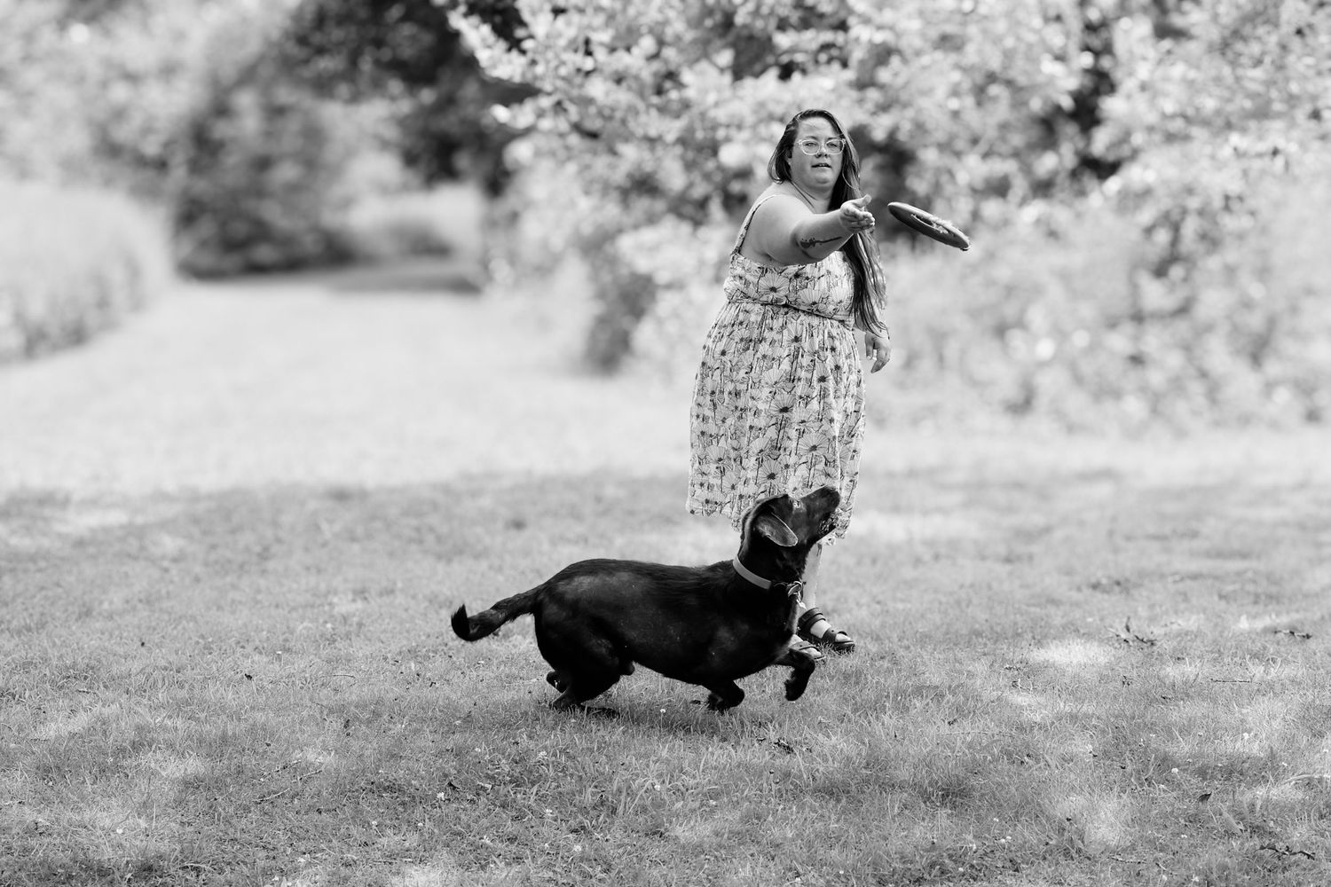 A joyful moment captured in black and white as someone dances in a floral dress while a playful dog runs nearby.