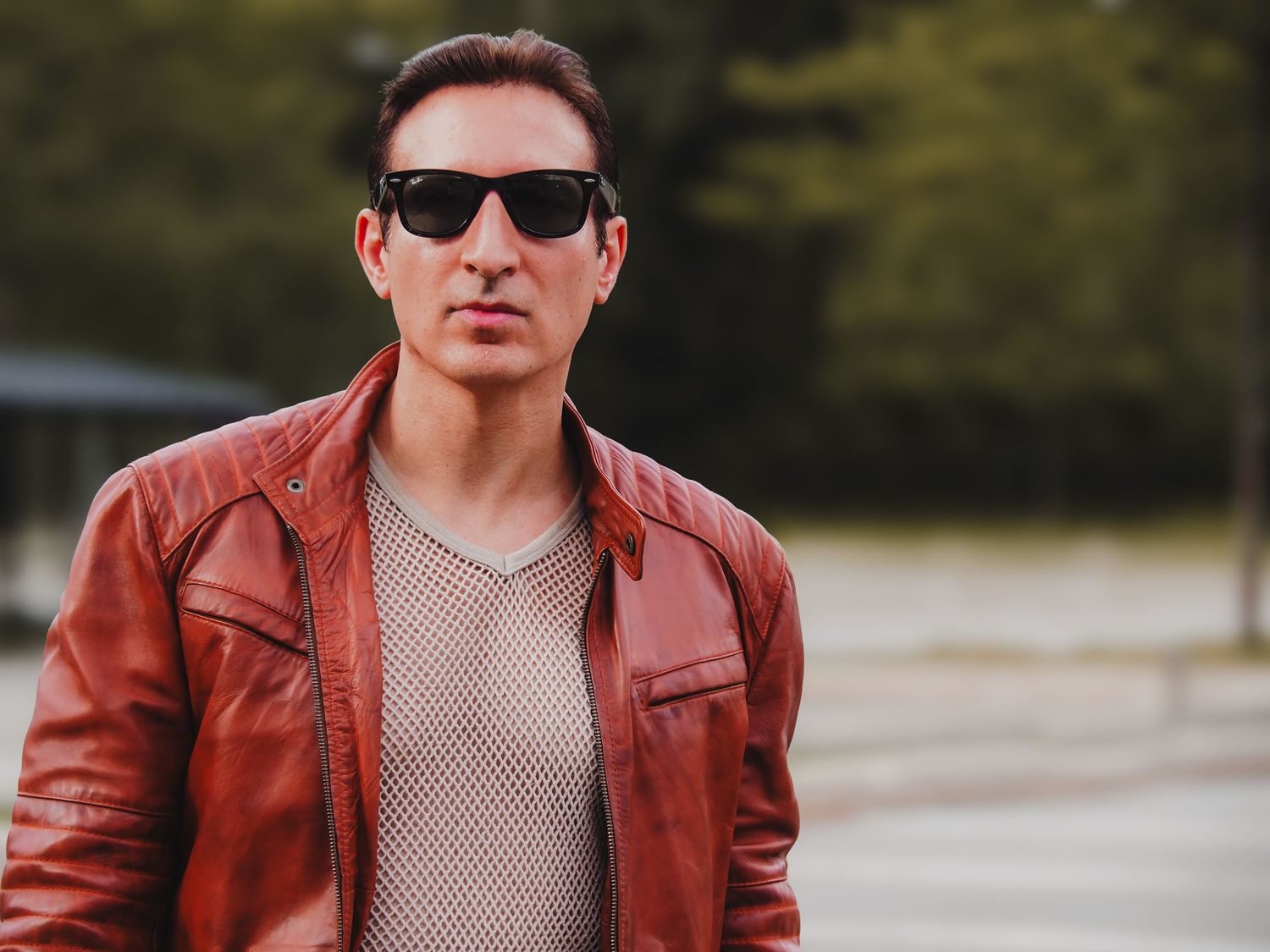 Person wearing sunglasses and red leather jacket poses outdoors in natural lighting.