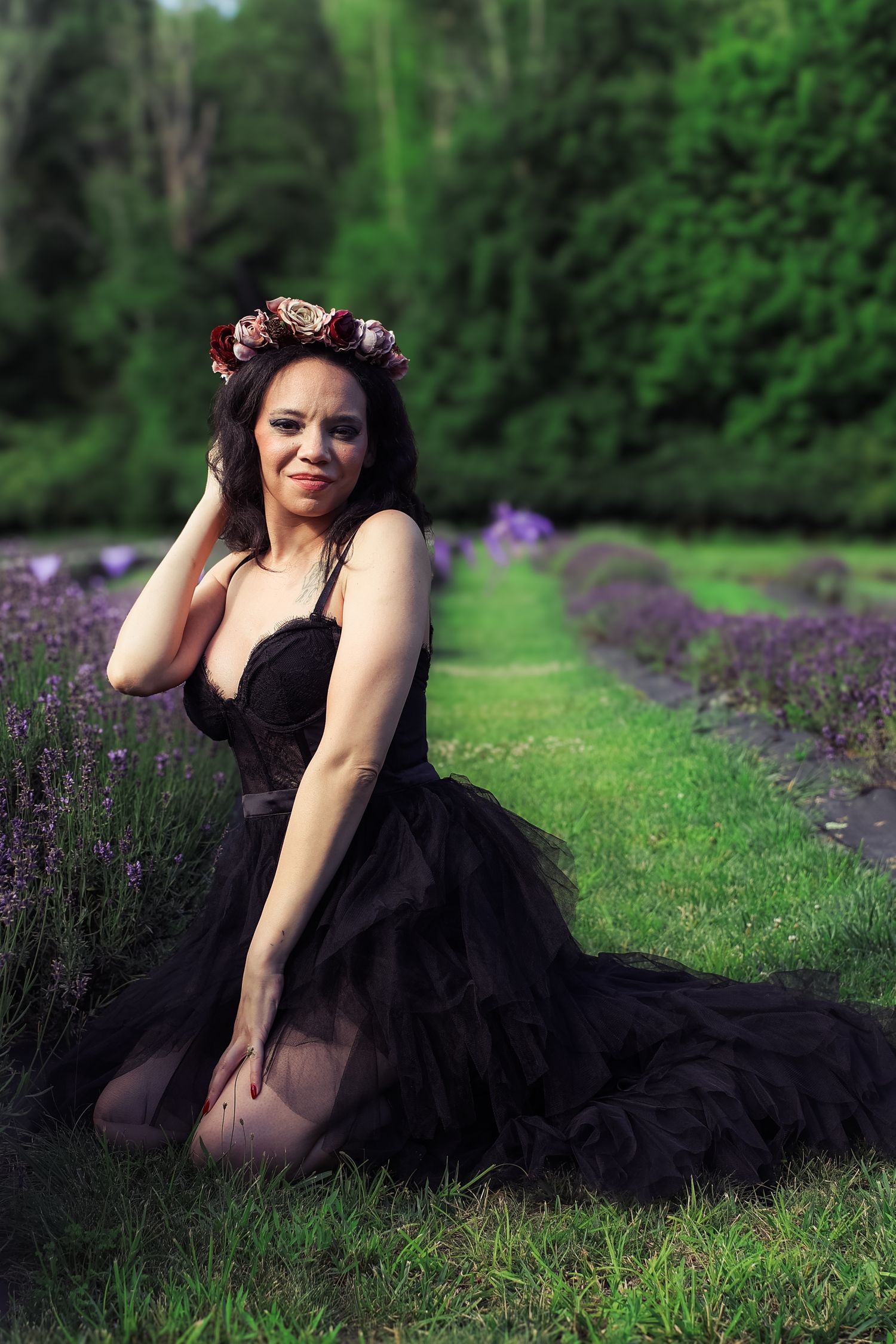 A figure in a black dress poses gracefully in a garden with purple flowers and lush greenery in the background.