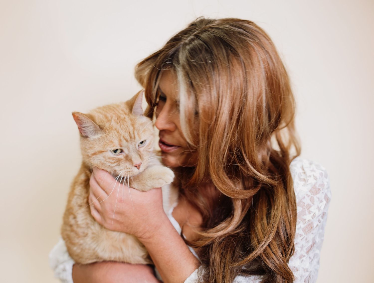 A ginger cat being affectionately held and petted while looking up with bright eyes.