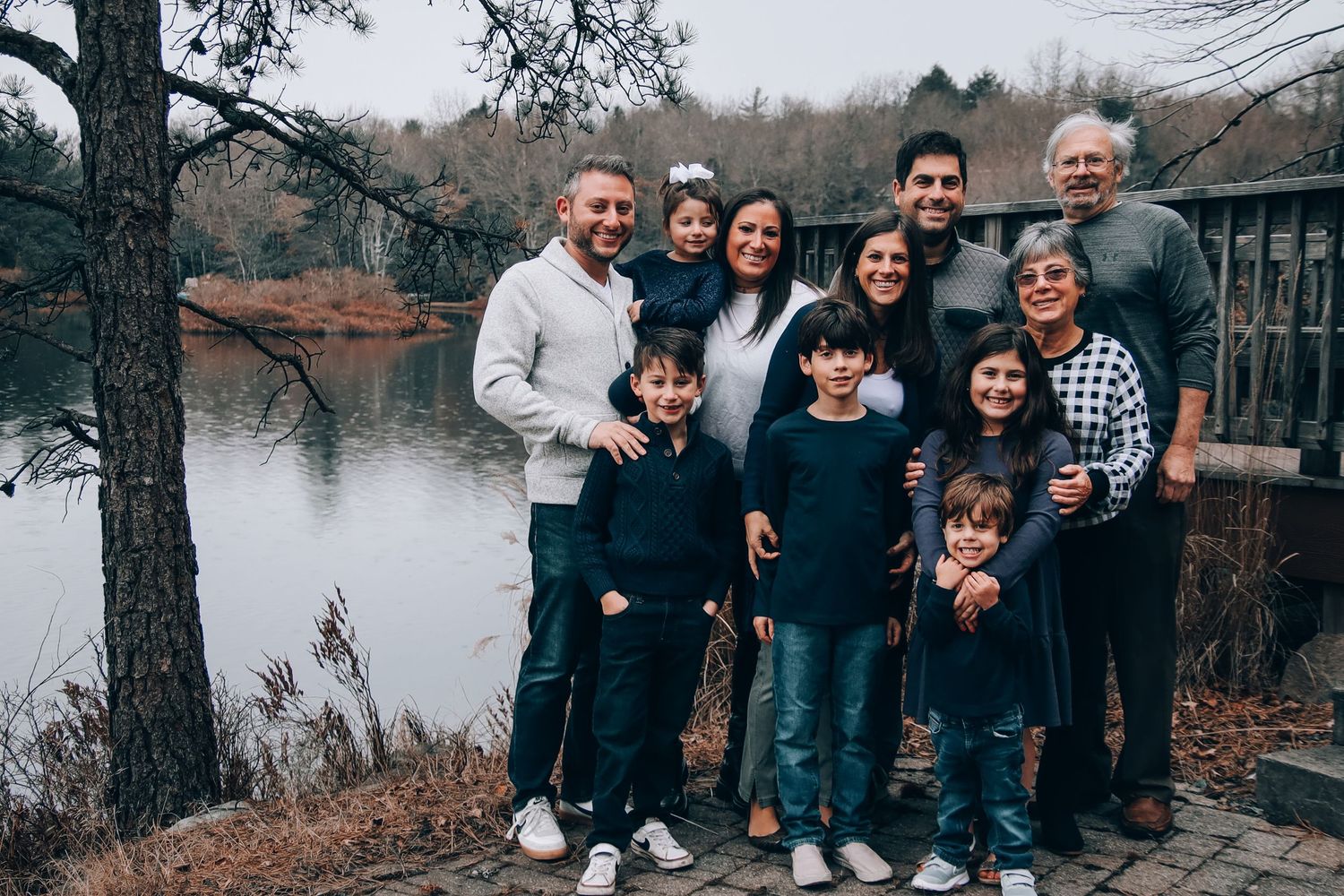 A group of people pose together outdoors near a lake on an overcast autumn day.