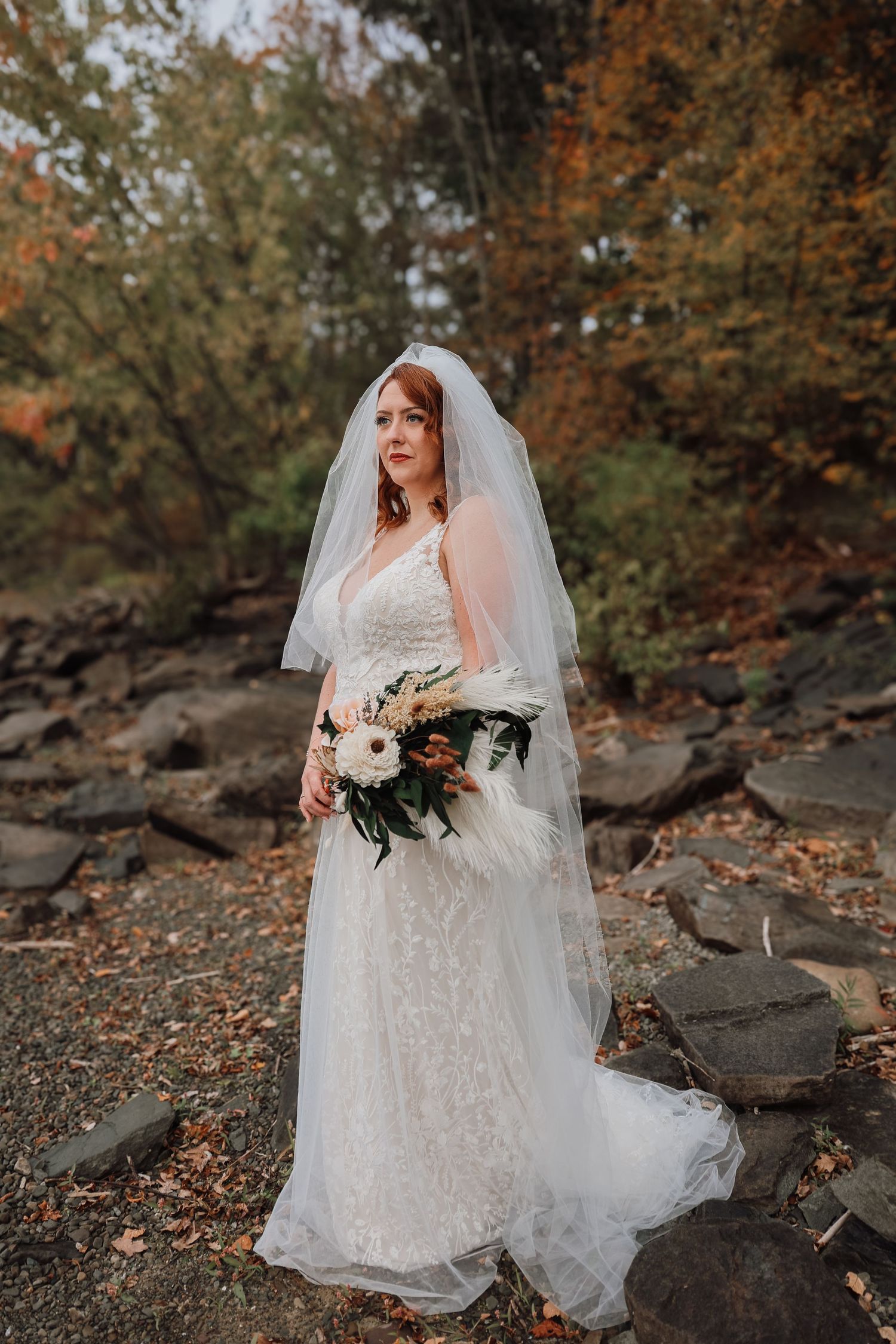 A bride in a sparkly white gown and veil poses among autumn leaves and rocky terrain during a fall wedding photoshoot.