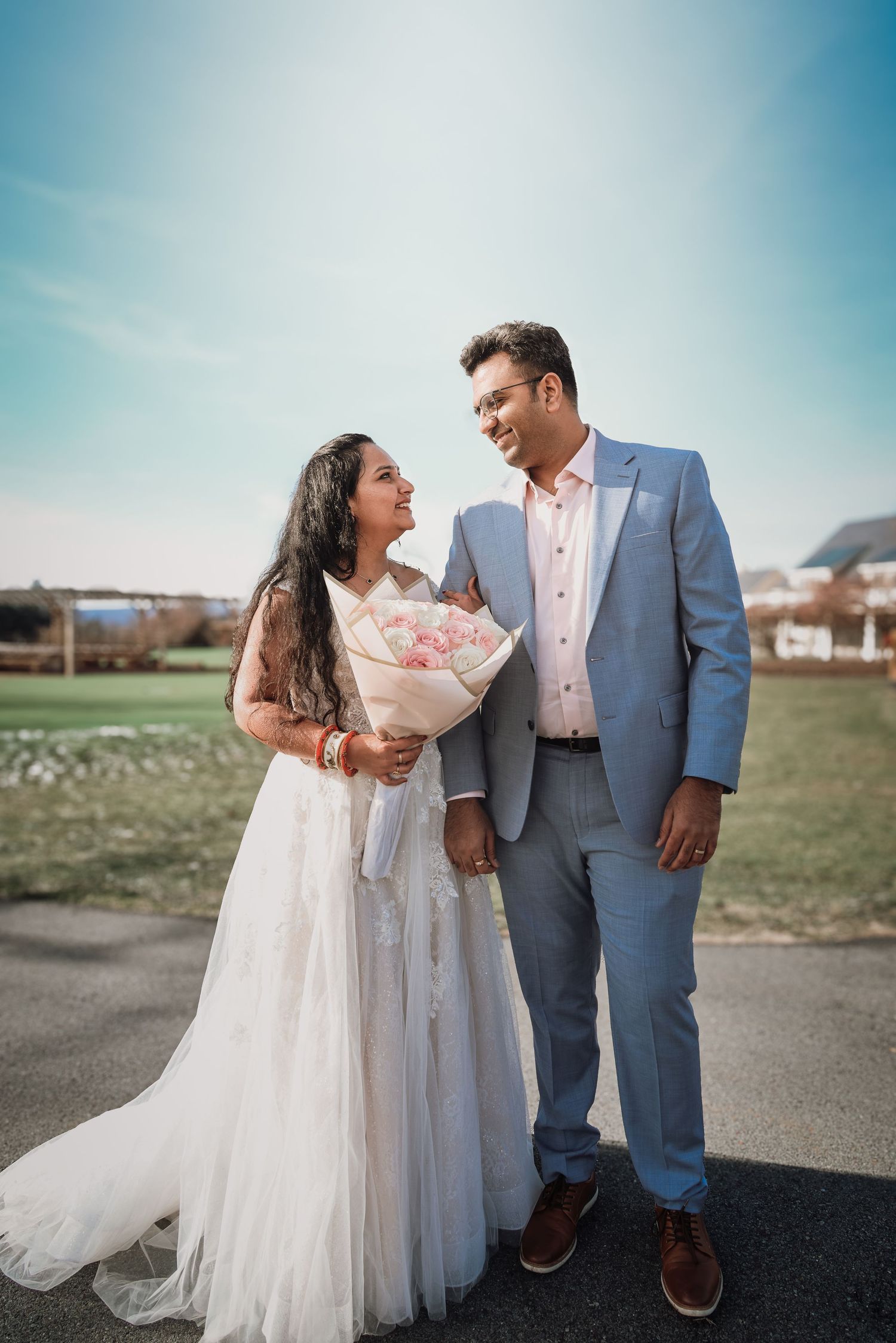 A couple in wedding attire shares a romantic moment together on a sunny day with blue skies in the background.