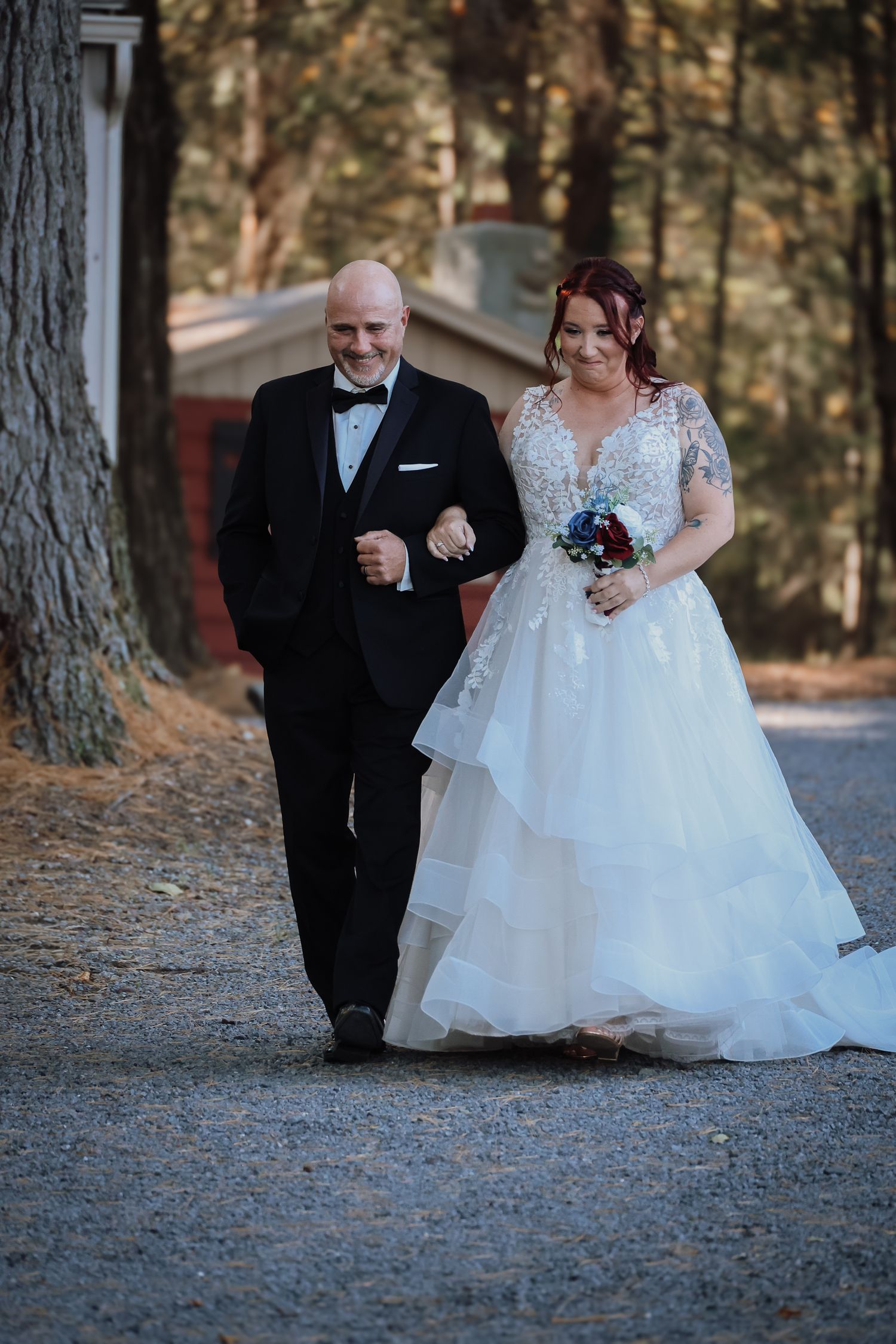 A couple in wedding attire walks together on a path through a wooded outdoor setting during their special day.
