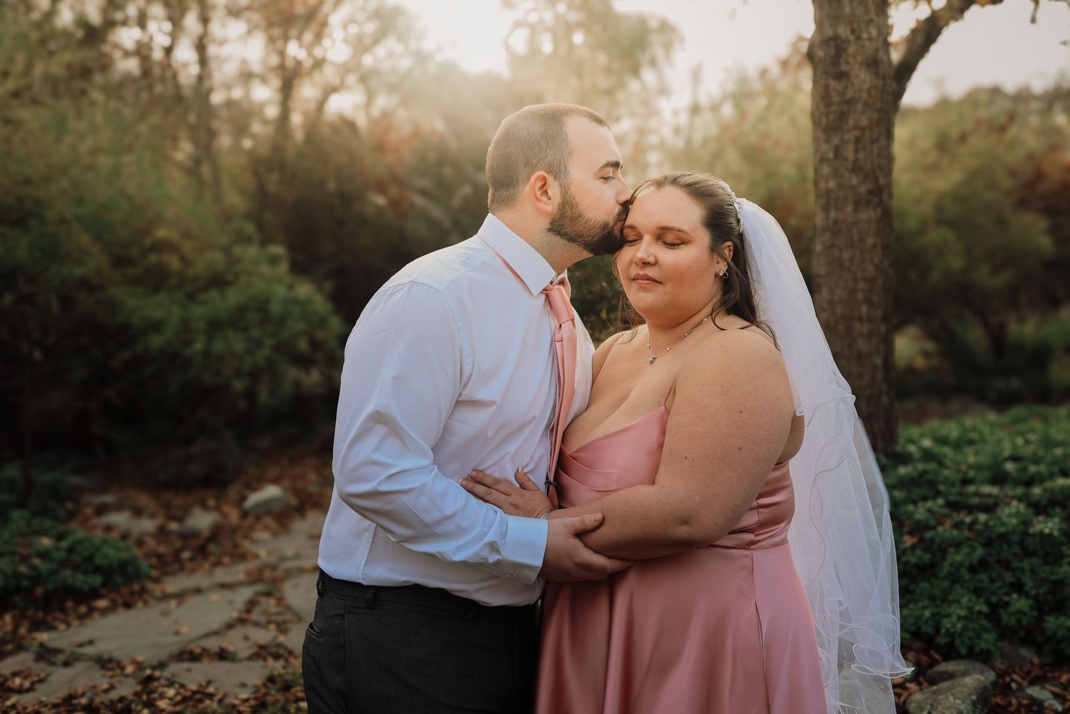 A romantic wedding couple embraces in a sunlit garden setting during golden hour photography session.