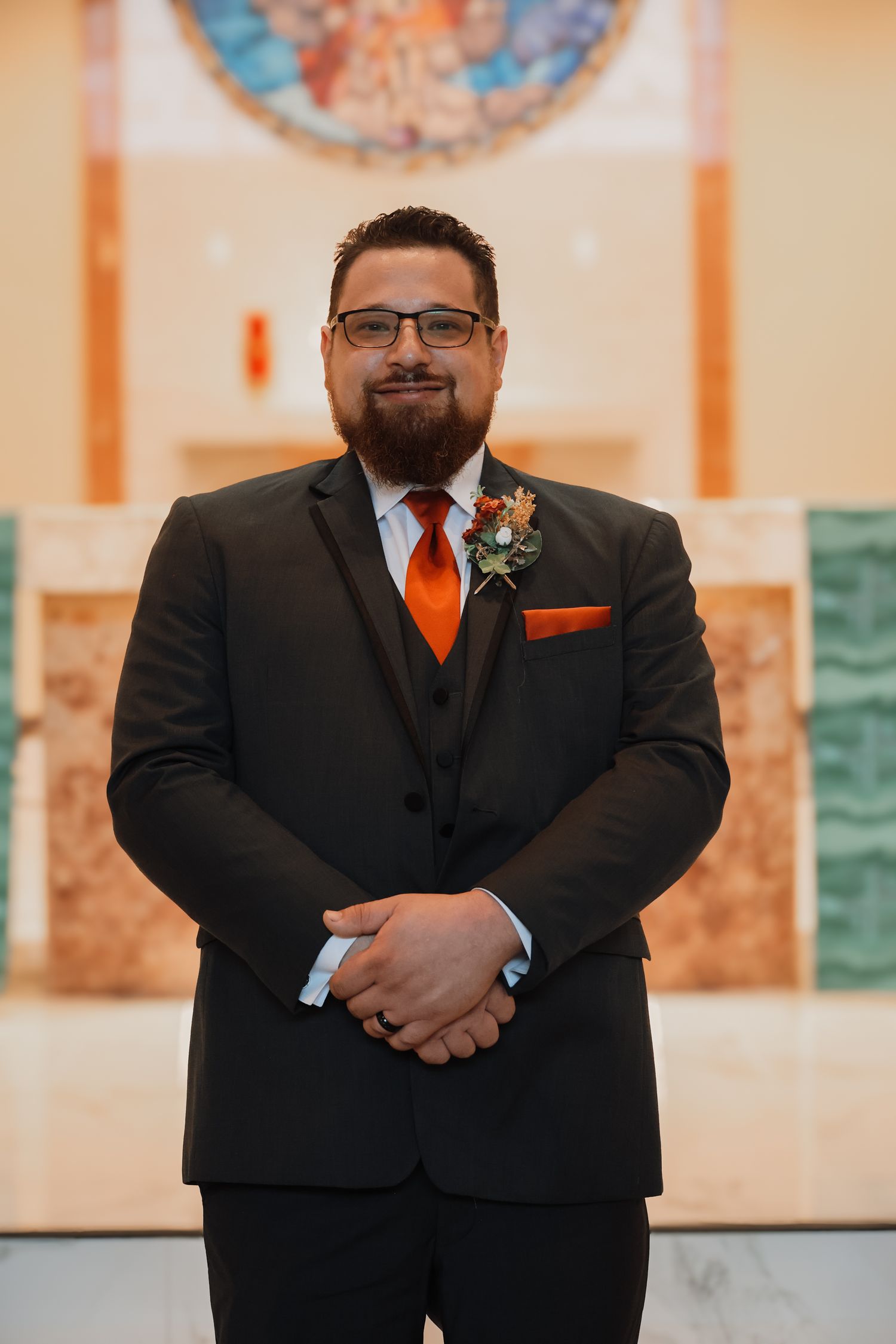 Groomsmen in black suits with orange accents stand together at a formal wedding ceremony.