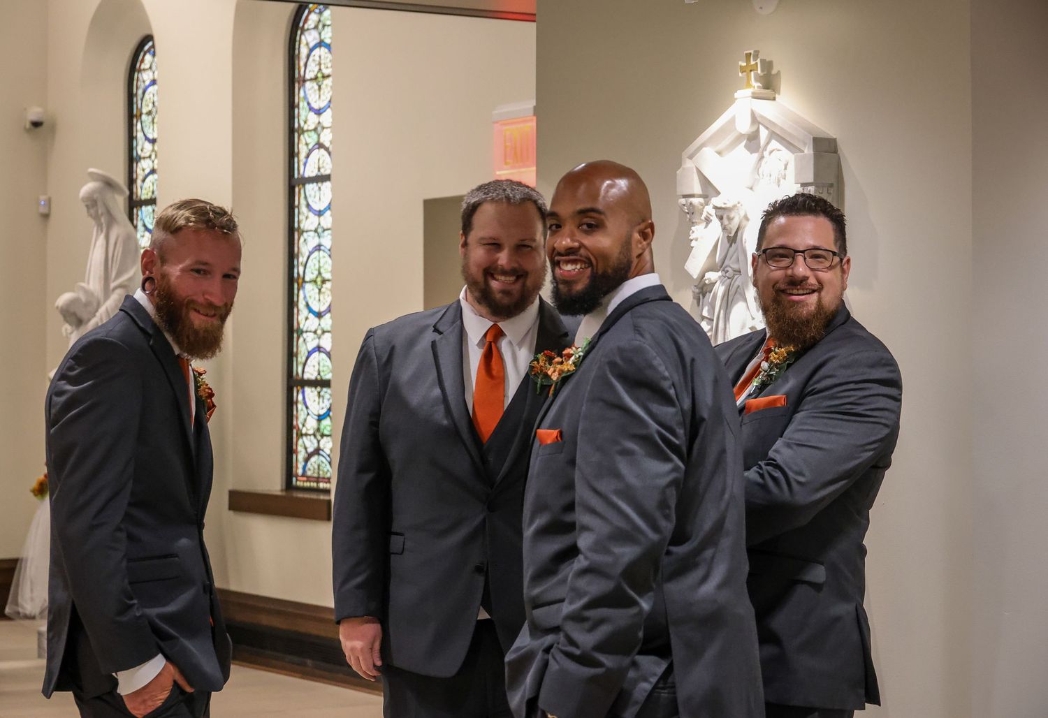 A group of people in formal attire gather in conversation inside a room with stained glass windows.