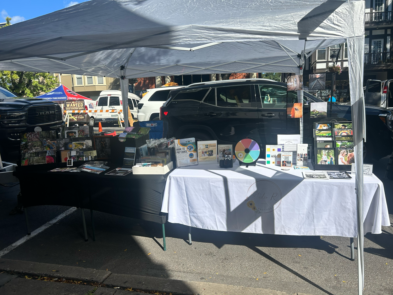 White canopy tents line up at an outdoor market with tables displaying various items for sale.