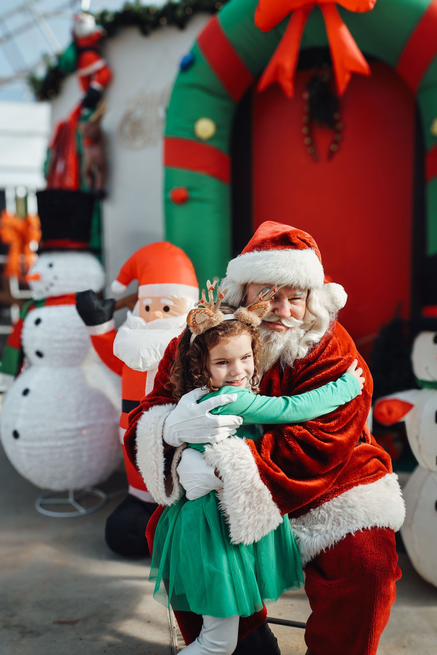 A festive holiday scene with Christmas decorations including a large green wreath and illuminated snowman figures.