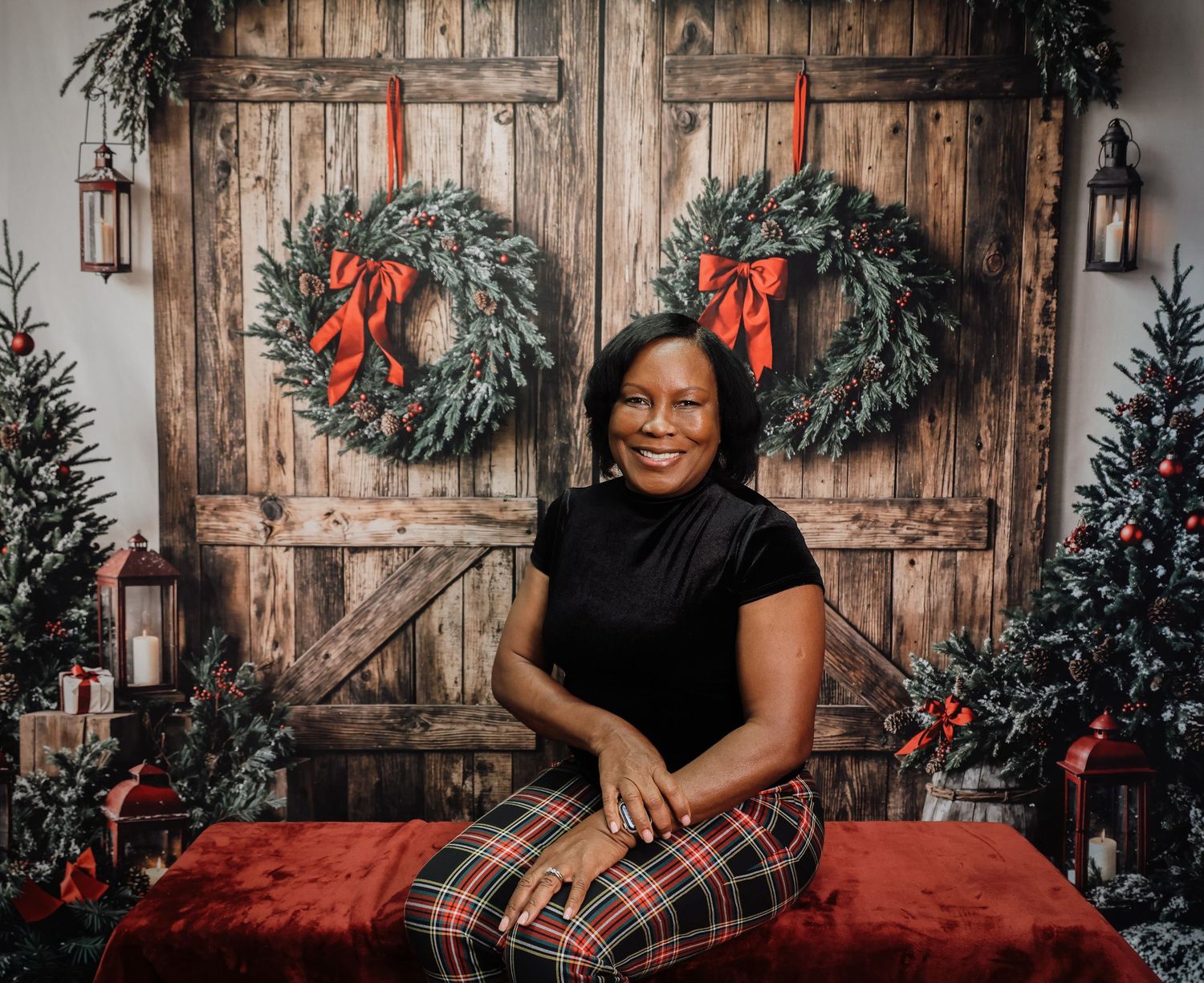 Holiday photo session with rustic wooden backdrop, evergreen garlands, red bows and plaid Christmas decor.