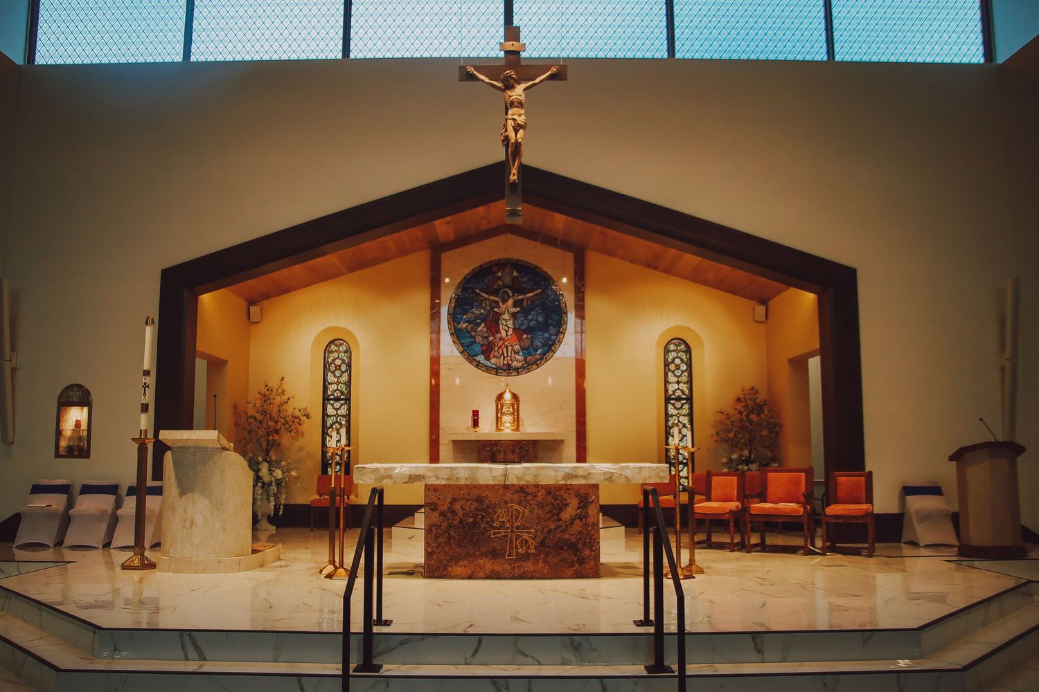 Interior view of a modern church sanctuary with blue stained glass windows and wooden pews illuminated by natural light.