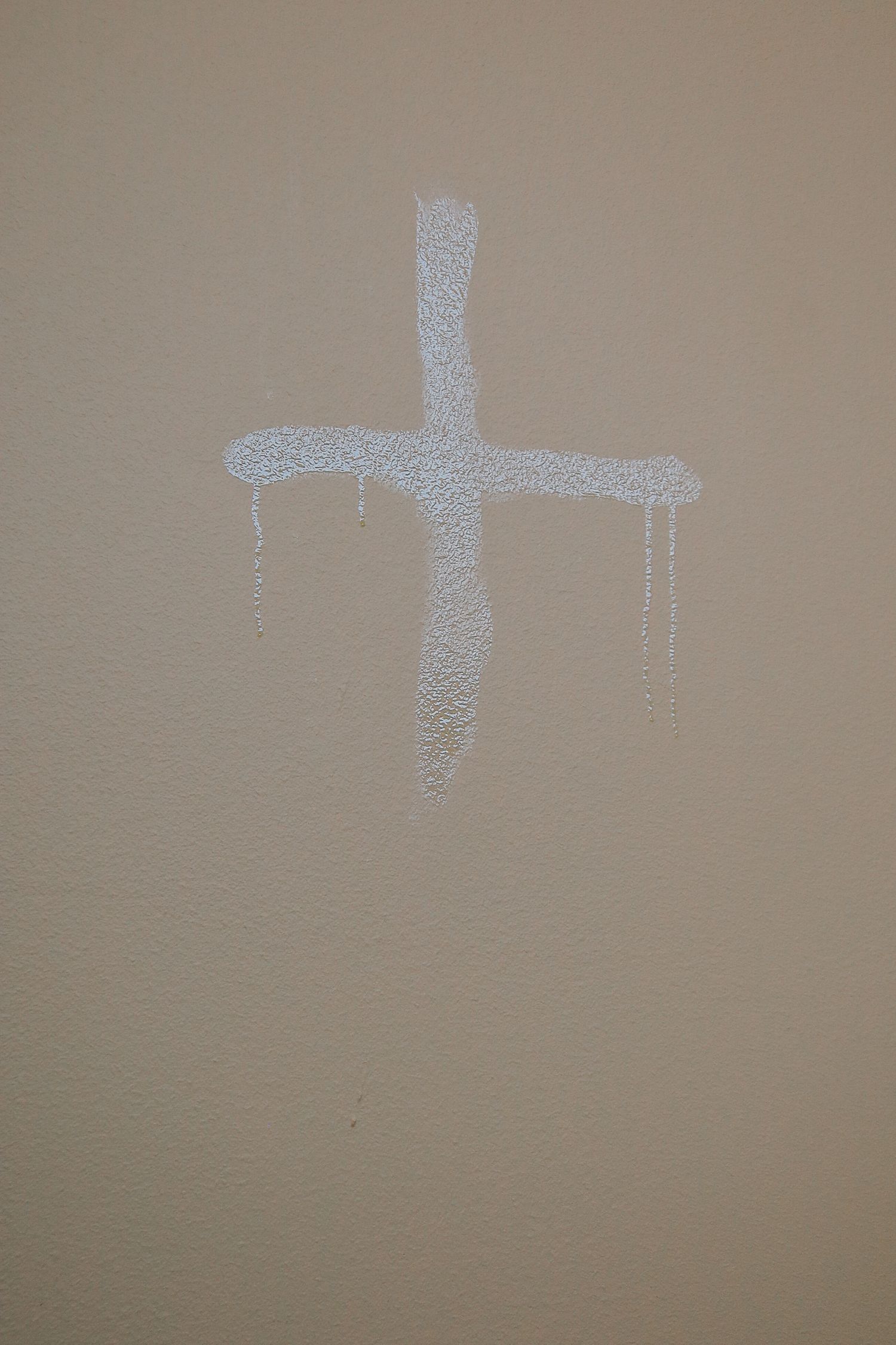 A series of identical cross symbols drawn in chalk or white paint fade progressively across a beige wall surface.