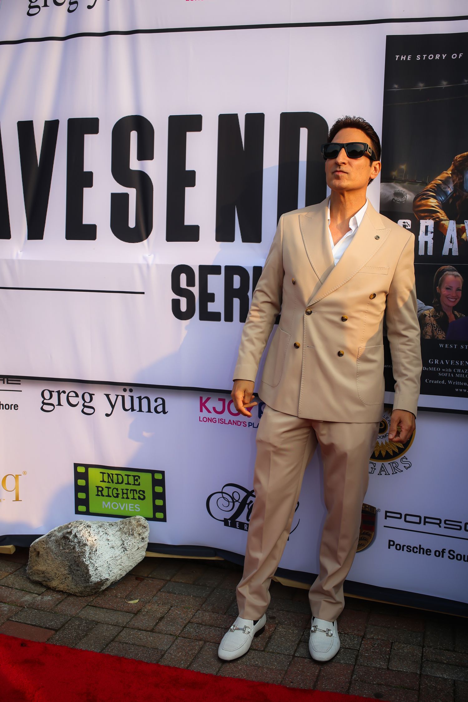 Four cropped views of someone wearing a beige suit and white sneakers posing against a promotional backdrop.