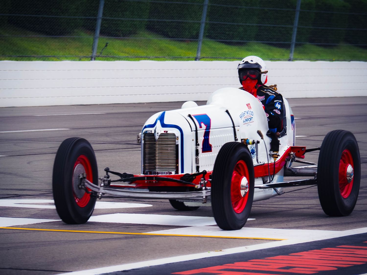 A vintage formula race car speeds along a racetrack with red and white curbing visible in the corner.