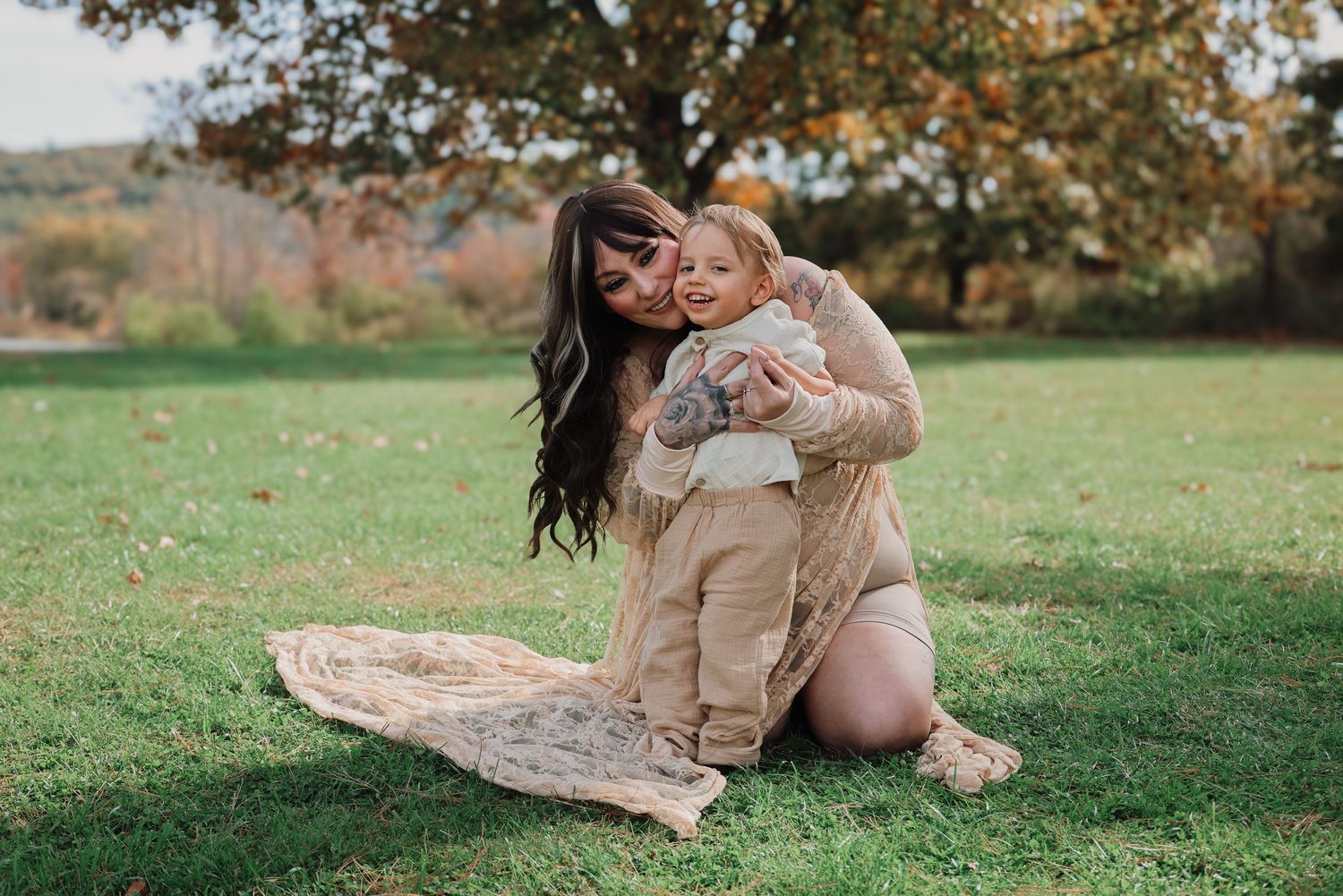 Mother and child sitting together on a blanket in a grassy field during autumn.