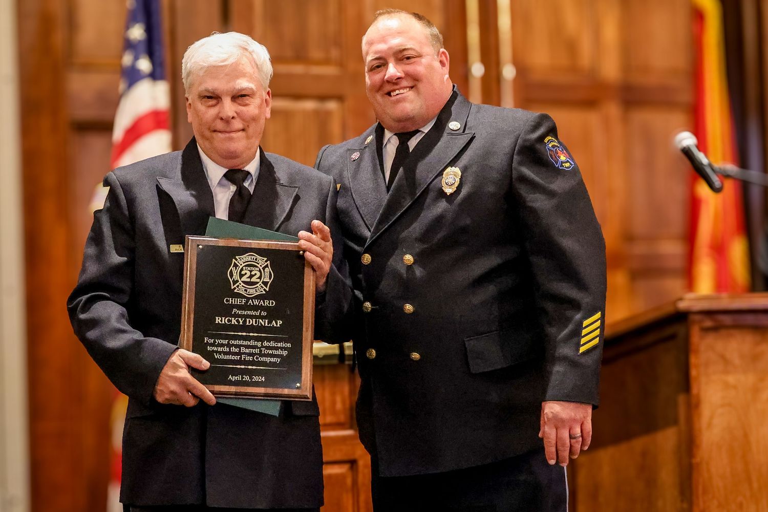 Two people in formal attire stand together at an awards ceremony with one holding a commemorative plaque.