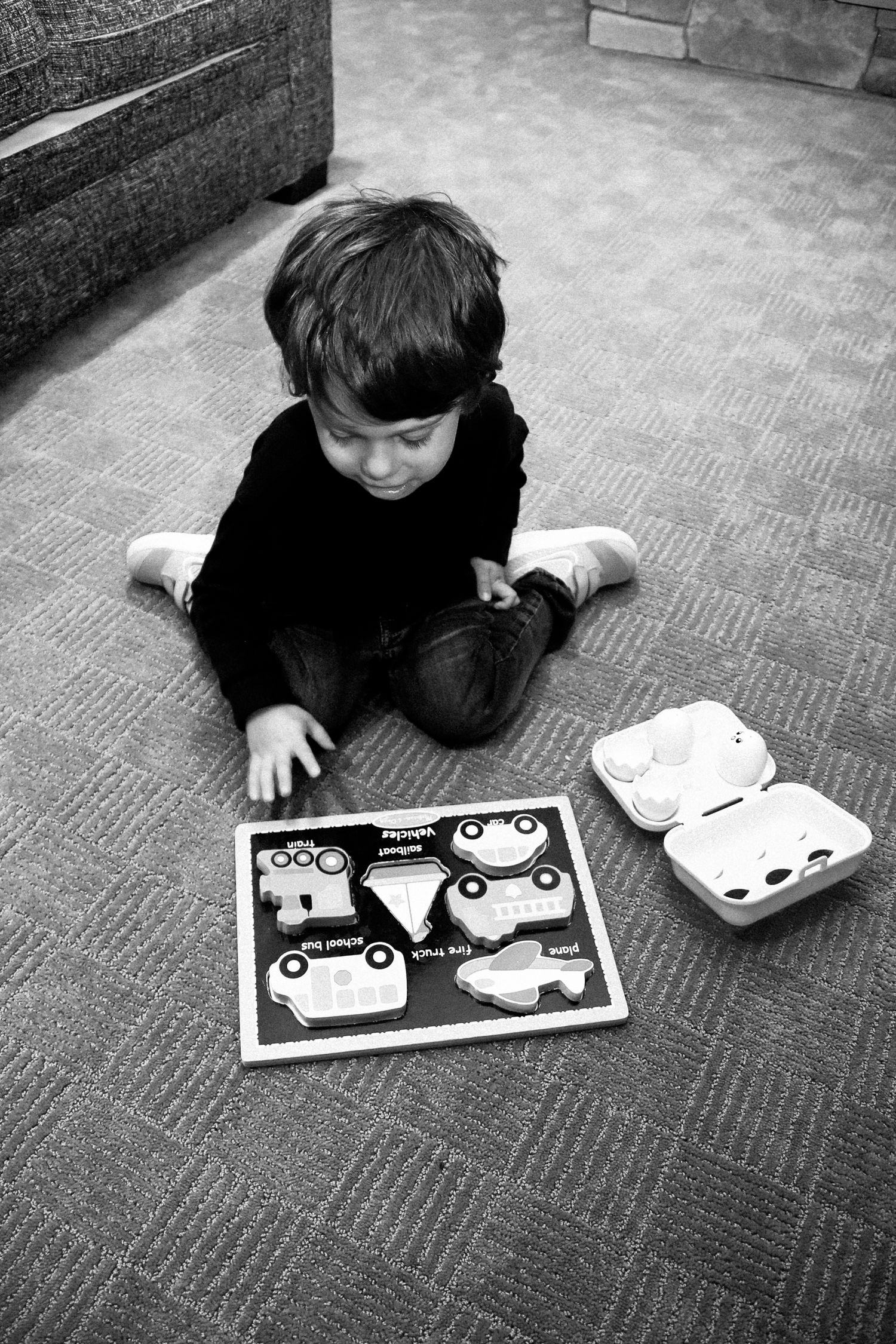 A child in black lies on carpet while looking at a book with cartoon characters in black and white.