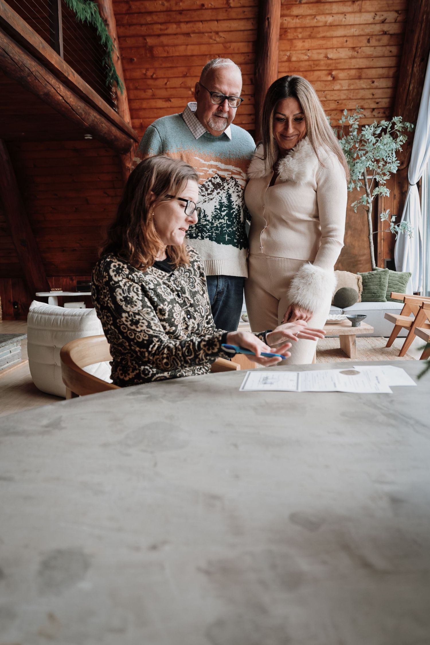 Group of people gathered around a table reviewing and signing documents in a room with exposed brick walls.