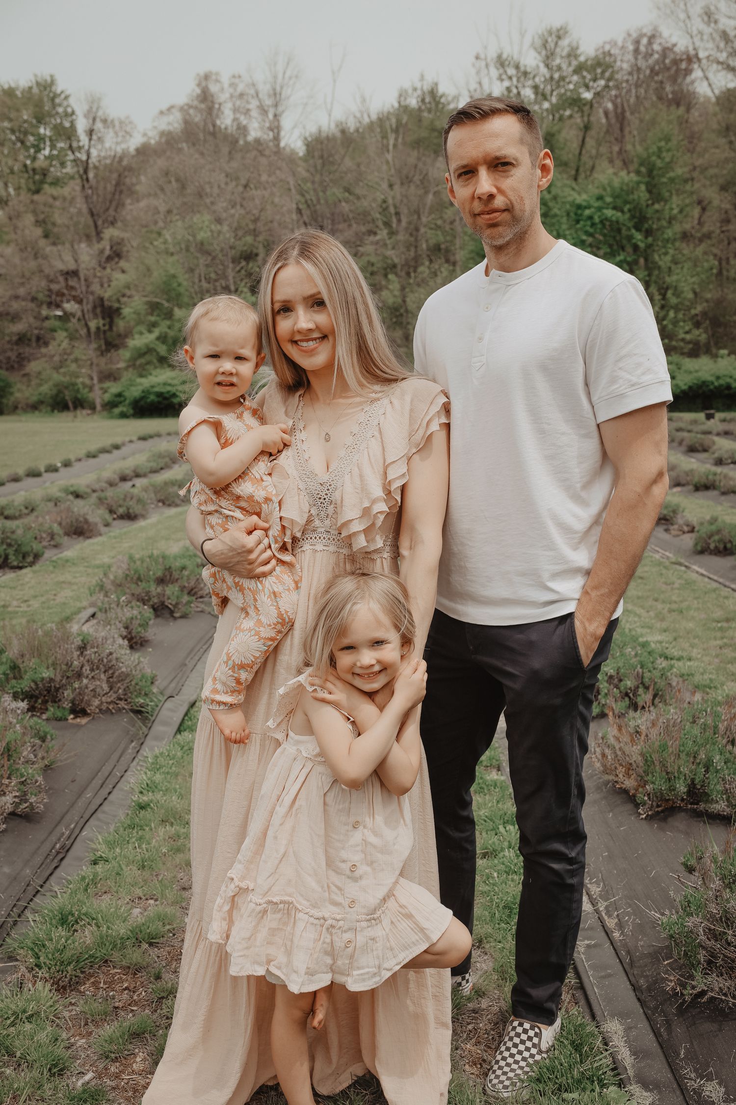 A family wearing coordinated cream and white outfits poses together on wooden planks in an outdoor garden setting.