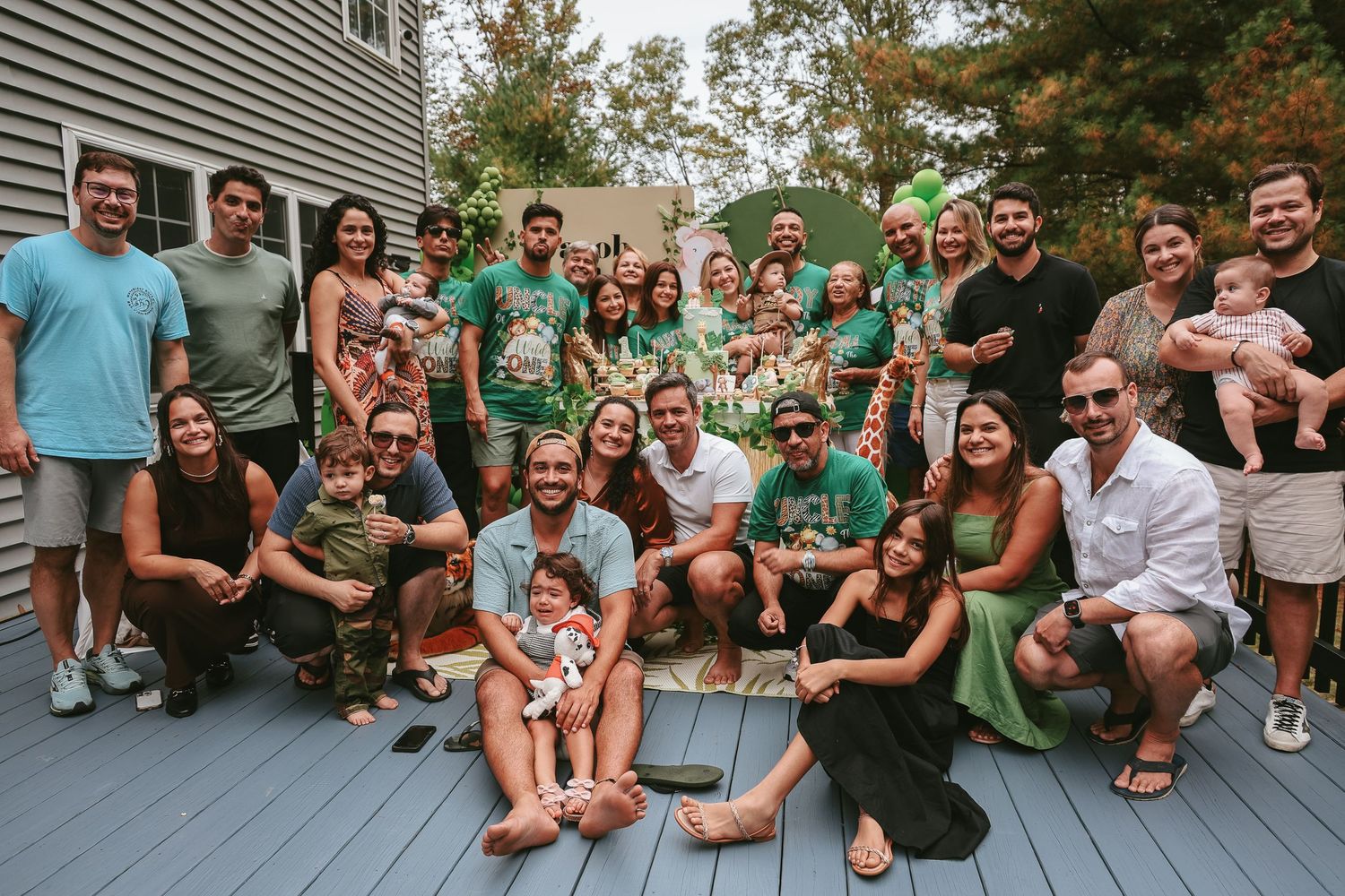 A large group wearing matching green shirts gathered together on an outdoor deck for a group photo.