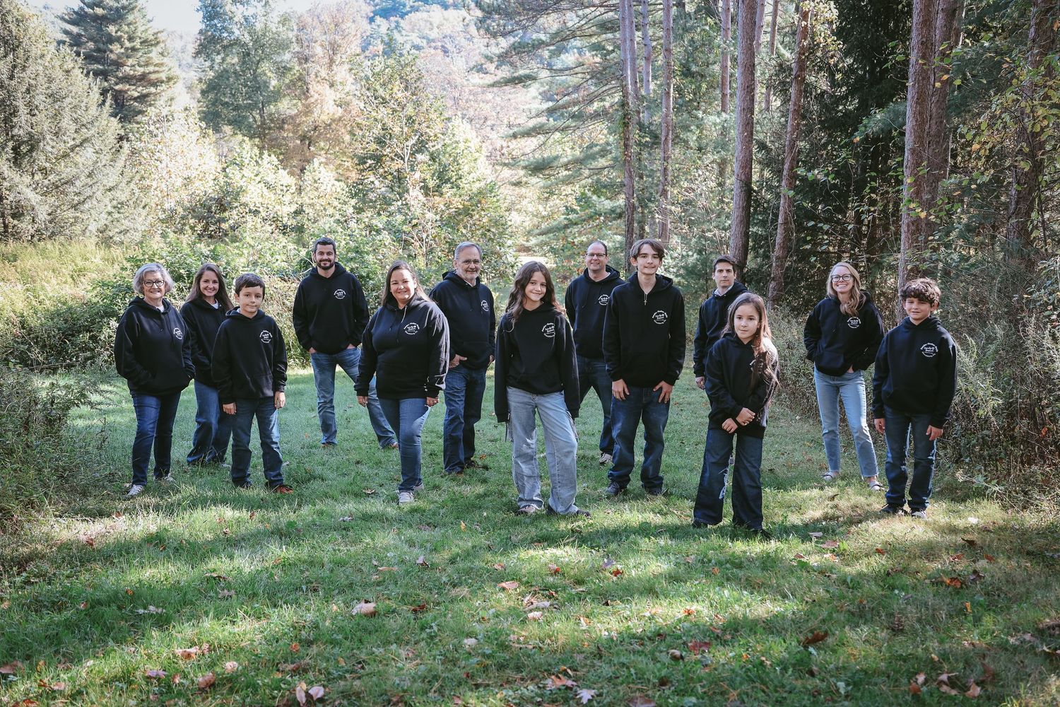 A group of people gathered outdoors in a wooded area on a sunny autumn day.