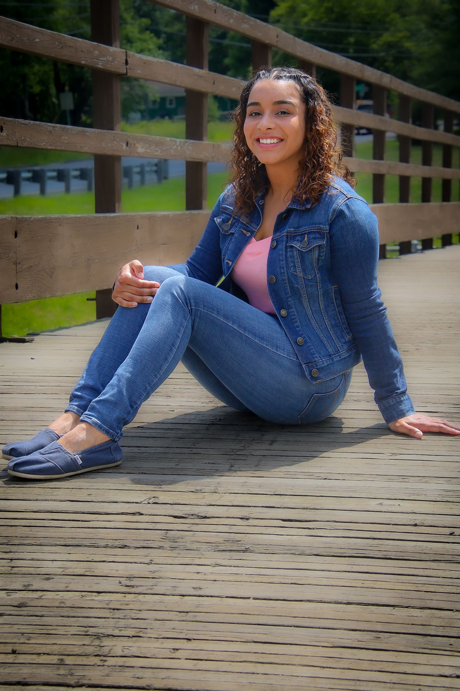Person in casual denim outfit relaxing on wooden deck surrounded by natural scenery.
