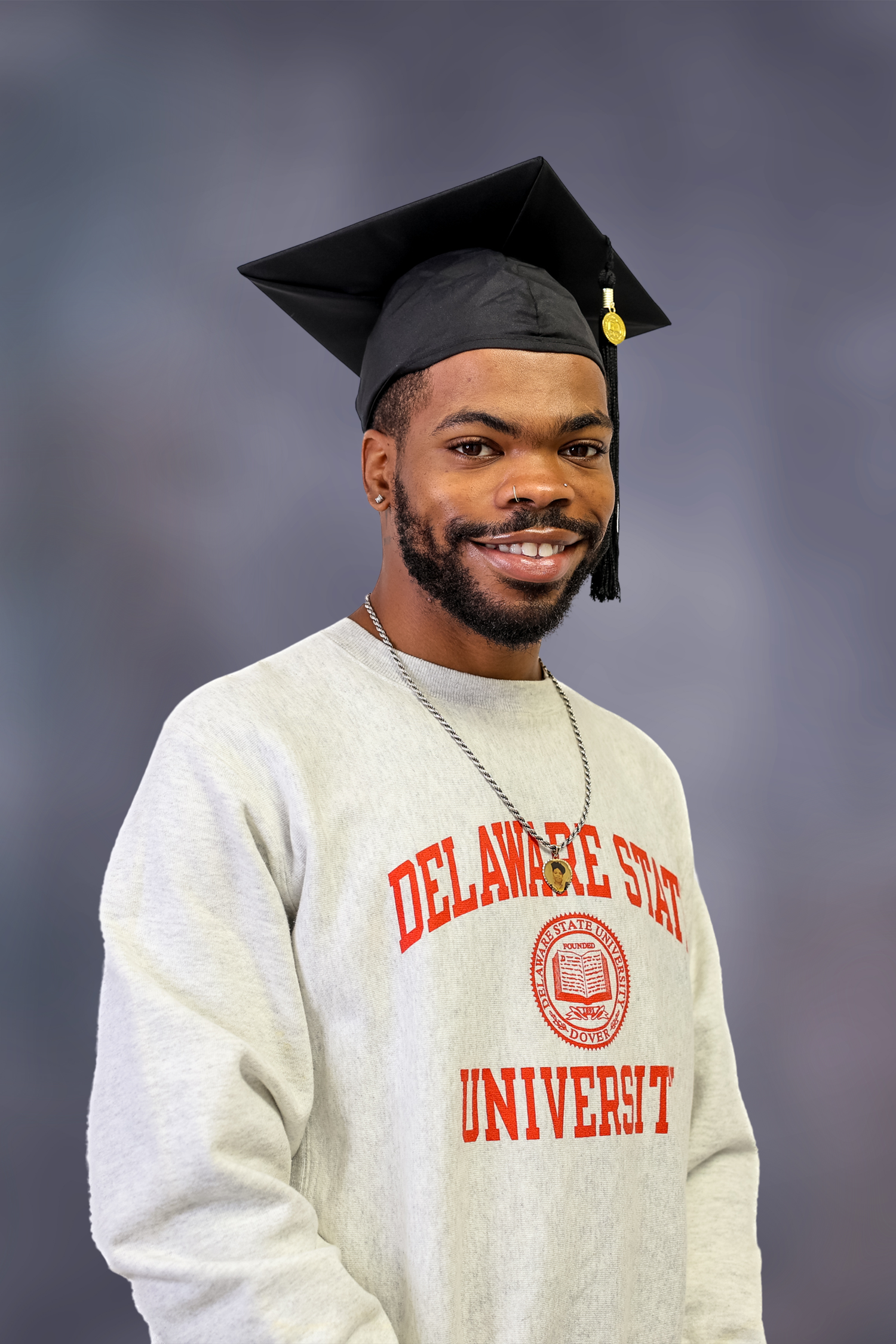 A graduate wearing a Delaware State University sweatshirt and black graduation cap smiles in a series of portraits.