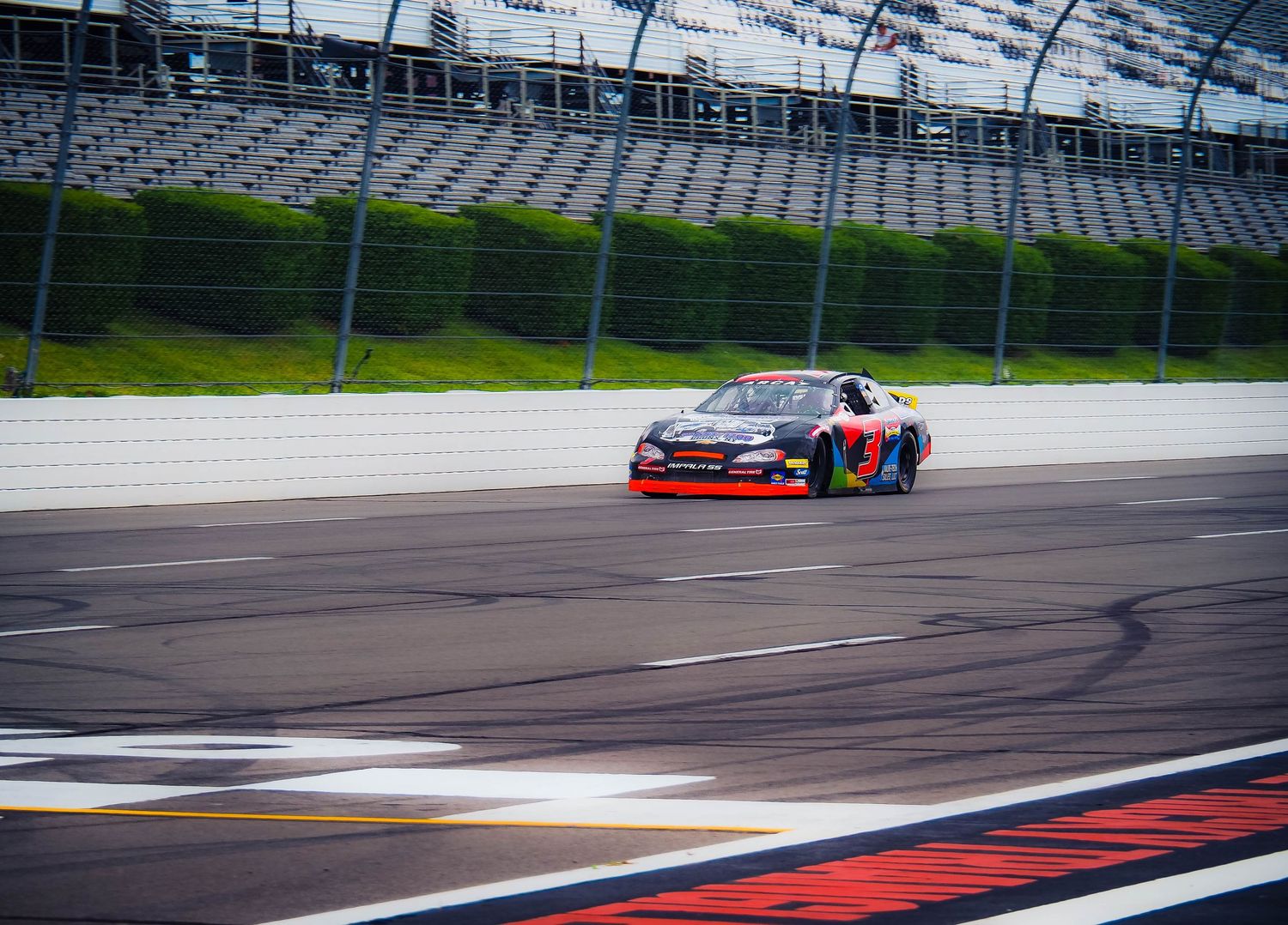 Race car drifts around track corner leaving dark tire marks on asphalt during motorsport competition.