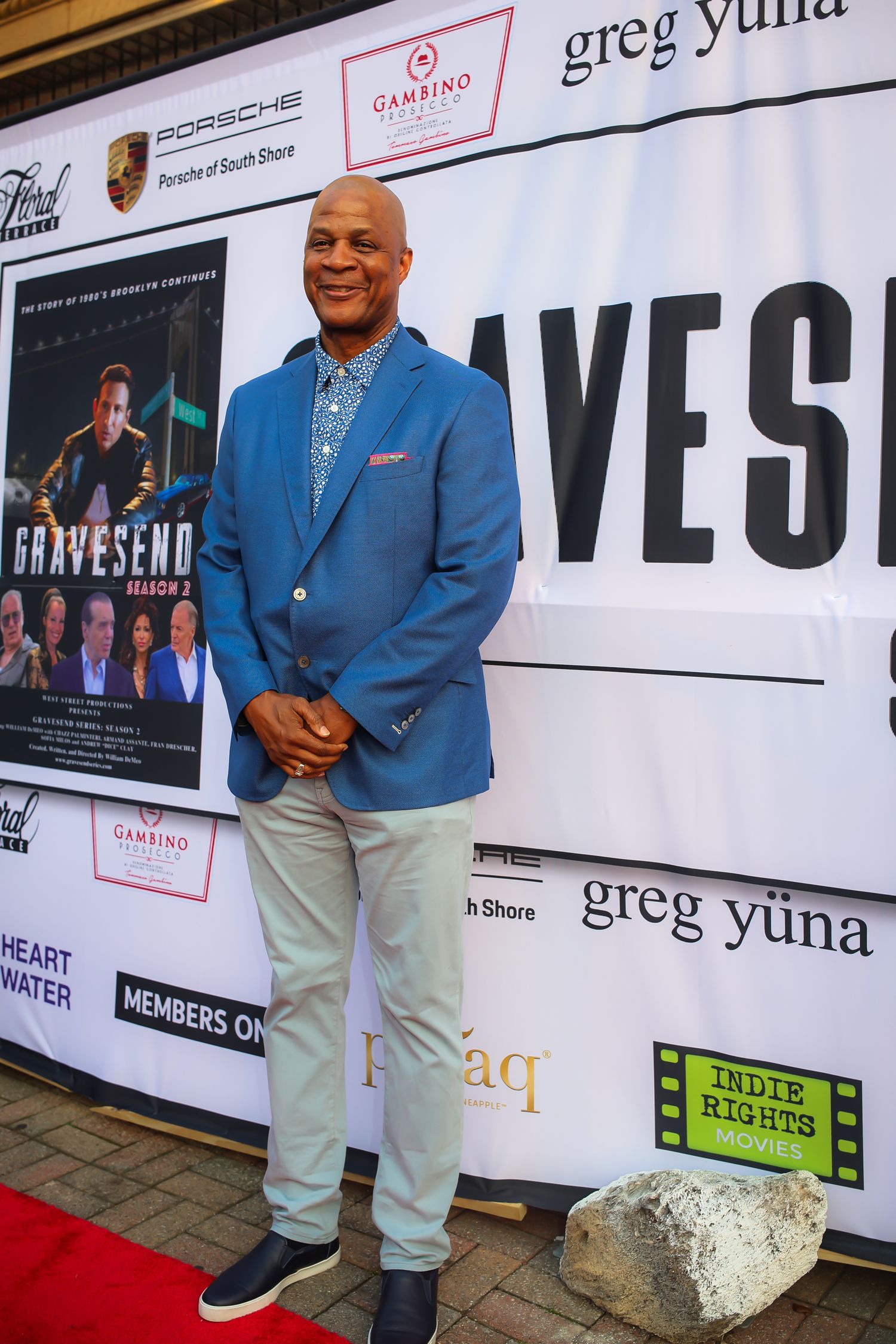 A person in a blue blazer and light pants stands in front of a promotional backdrop with various brand logos and text.