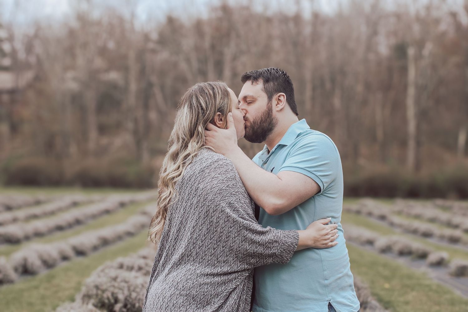 A couple shares a tender embrace while standing in a lavender field on an overcast day.