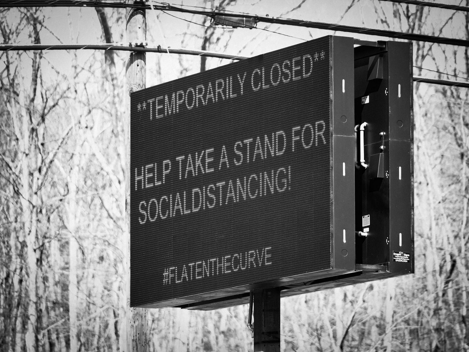 A digital sign displays 'Temporarily Closed' and 'Help Take A Stand For Social Distancing' with #FlattenTheCurve hashtag.