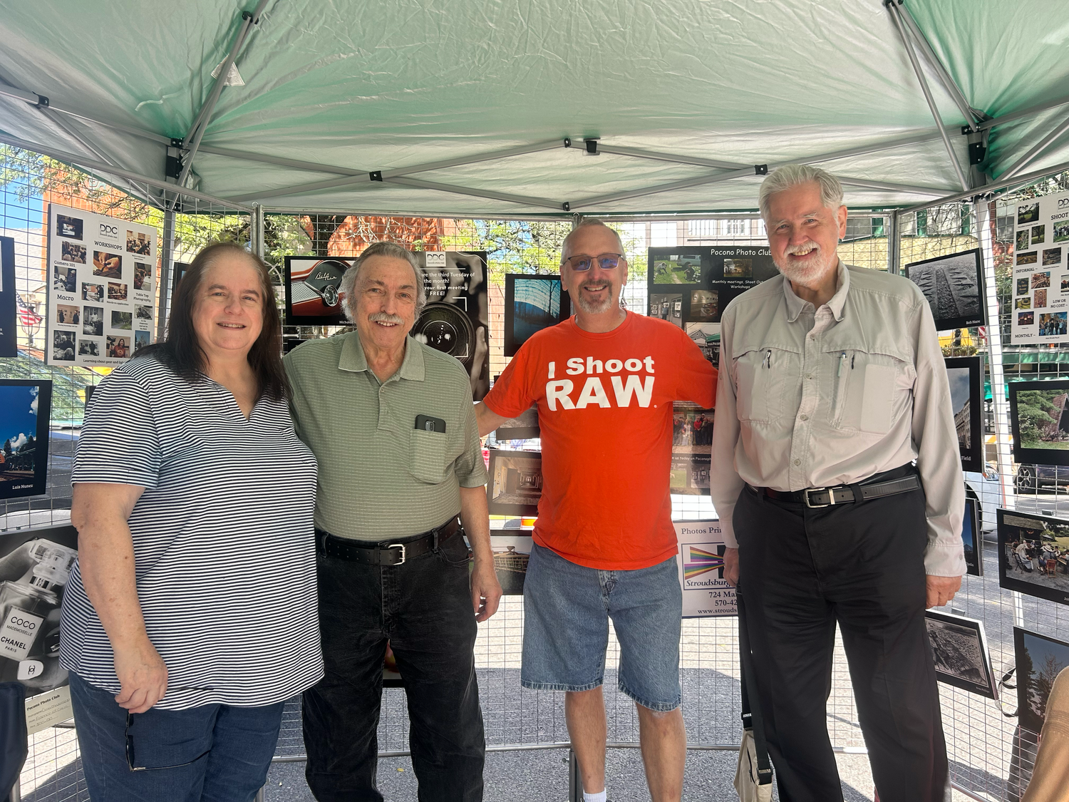 People gather at outdoor event booths with photo displays and informational materials displayed under tents.
