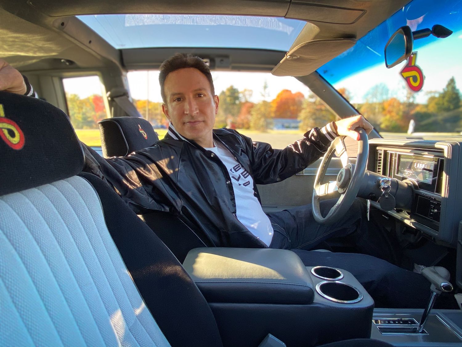 Interior view of a modern car with light blue leather seats and sunroof, captured during autumn with fall foliage visible outside.