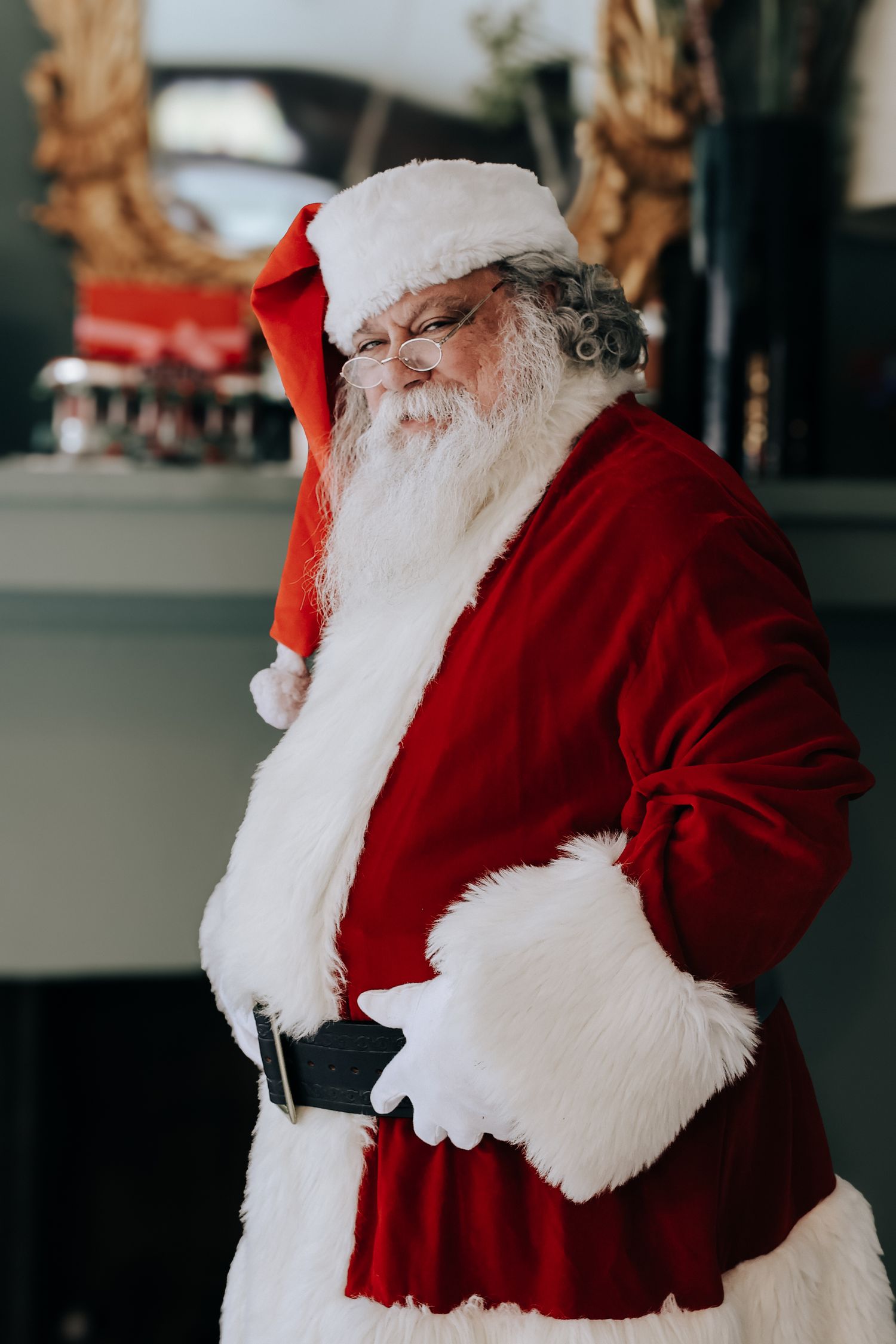 Santa Claus in traditional red suit and white beard laughs heartily in a festive holiday setting.