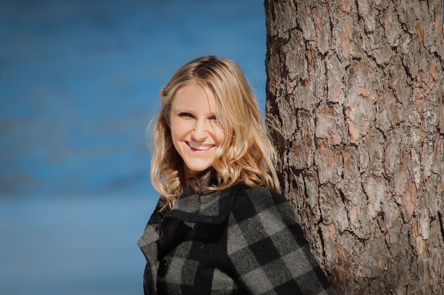 Woman in black and white buffalo plaid flannel poses against tree trunk in outdoor portrait series.