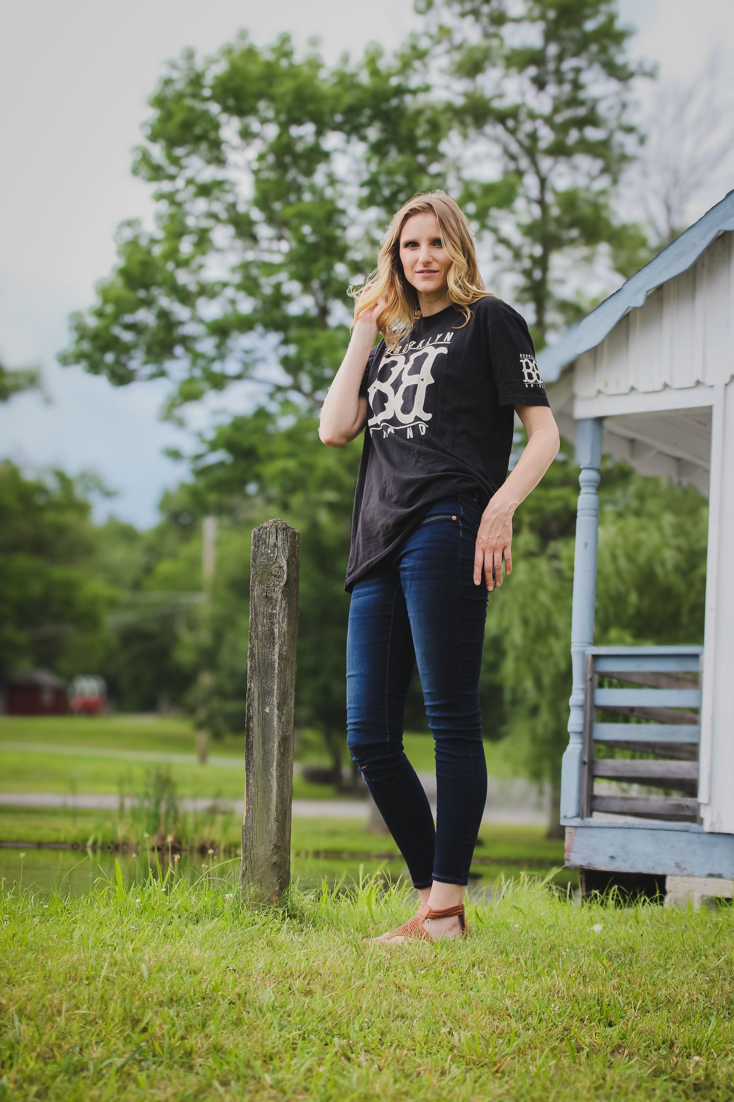 Casual outdoor portrait of someone wearing a black graphic t-shirt and skinny jeans standing by a rustic wooden post.