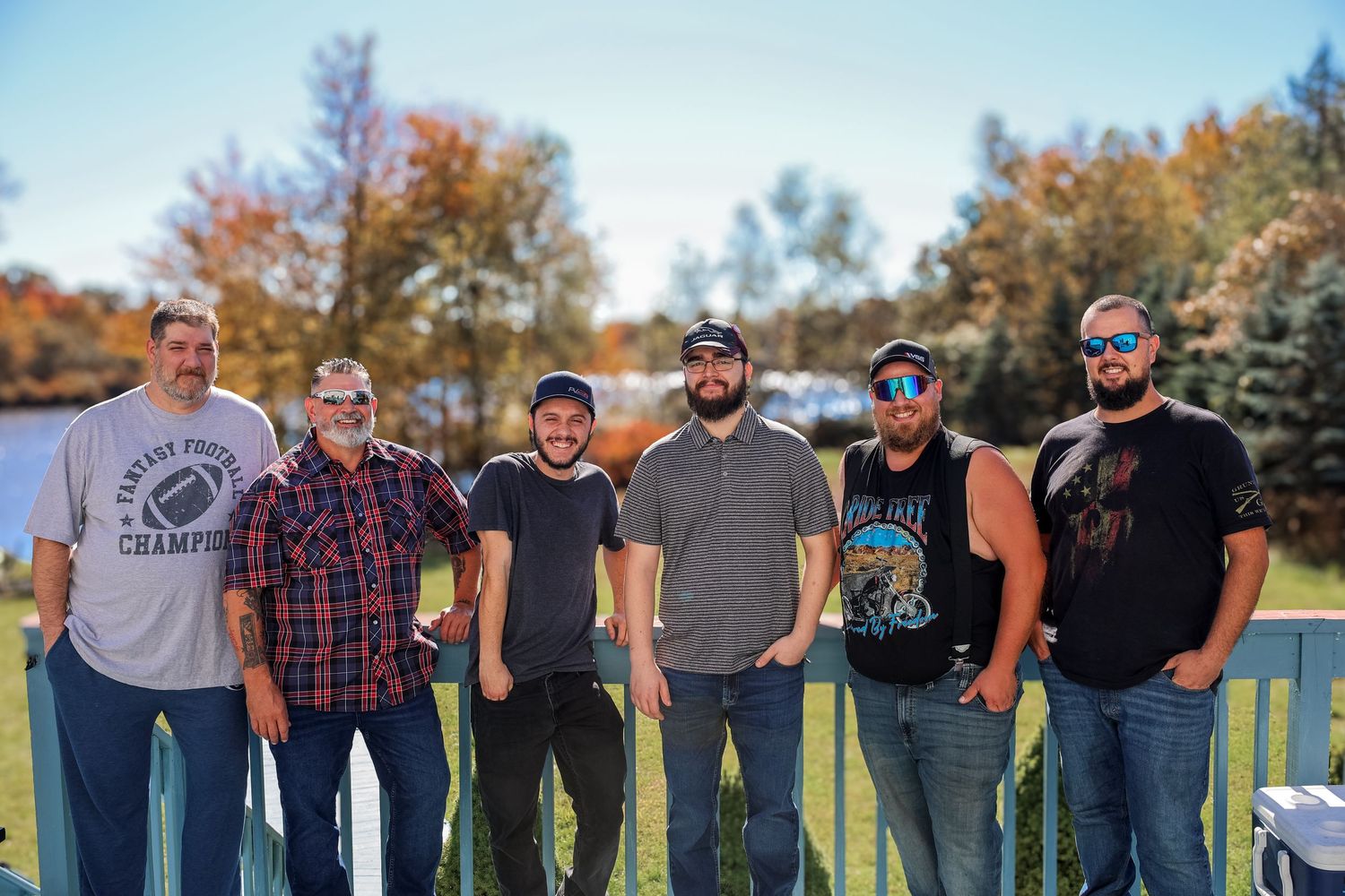 A group of people standing in a line outdoors on grass with trees in the background during autumn.