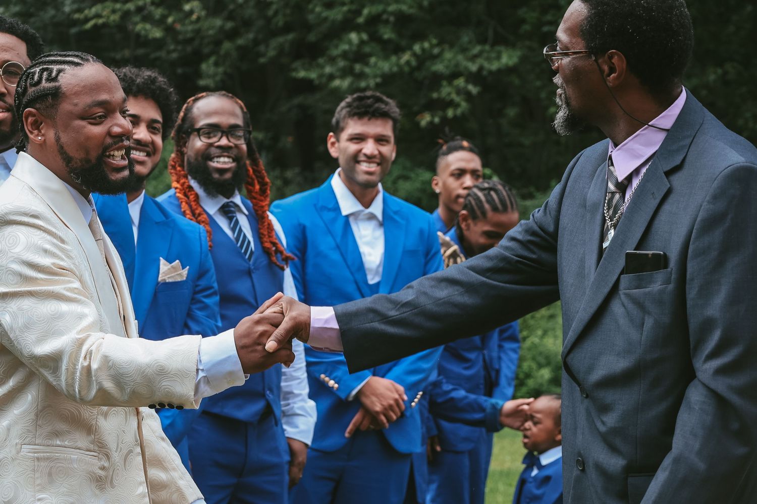 A group of people in formal attire and blue jackets stand together at an outdoor gathering.