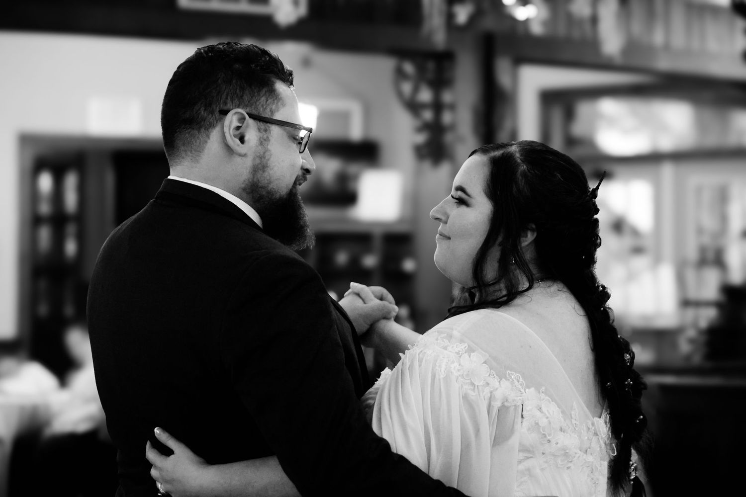 A couple shares a romantic dance at their wedding reception, surrounded by soft lighting and other guests.