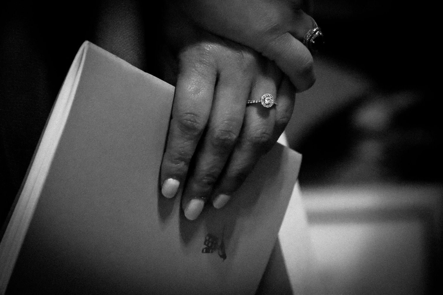 A hand wearing rings holds the corner of a book in black and white photography.