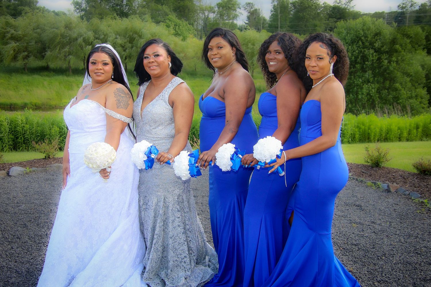 A bridal party poses together outdoors wearing coordinated white and royal blue dresses.
