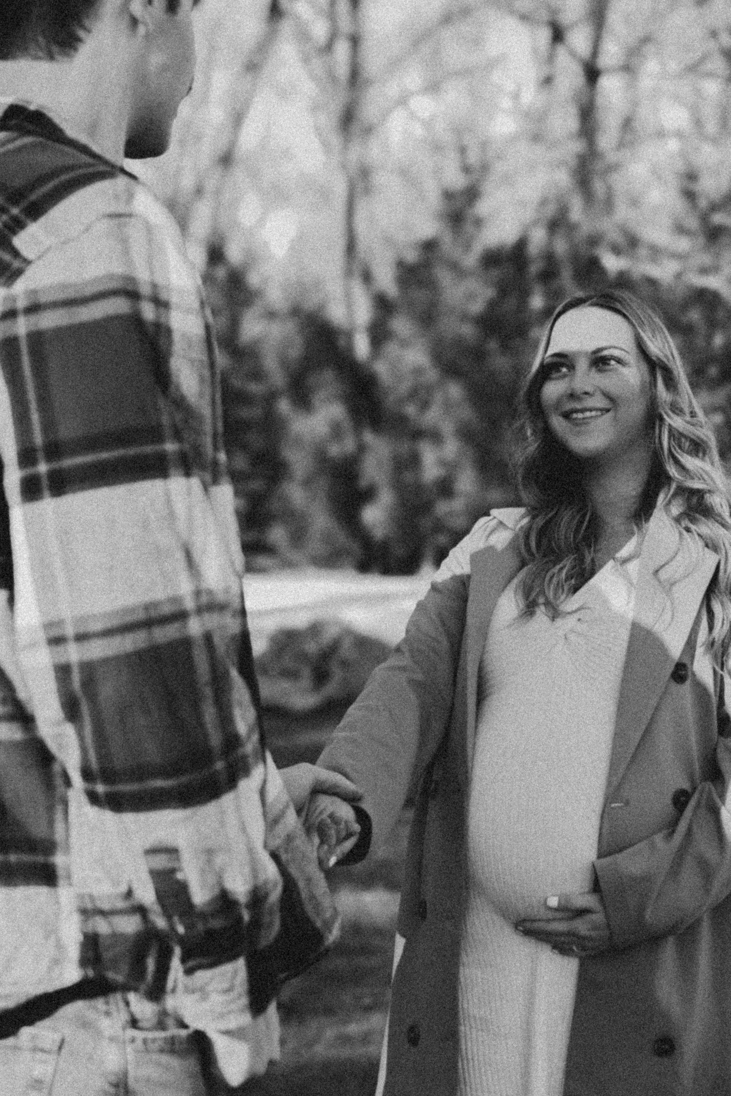 A couple shares laughter during an outdoor engagement photo session wearing cozy fall attire in black and white.