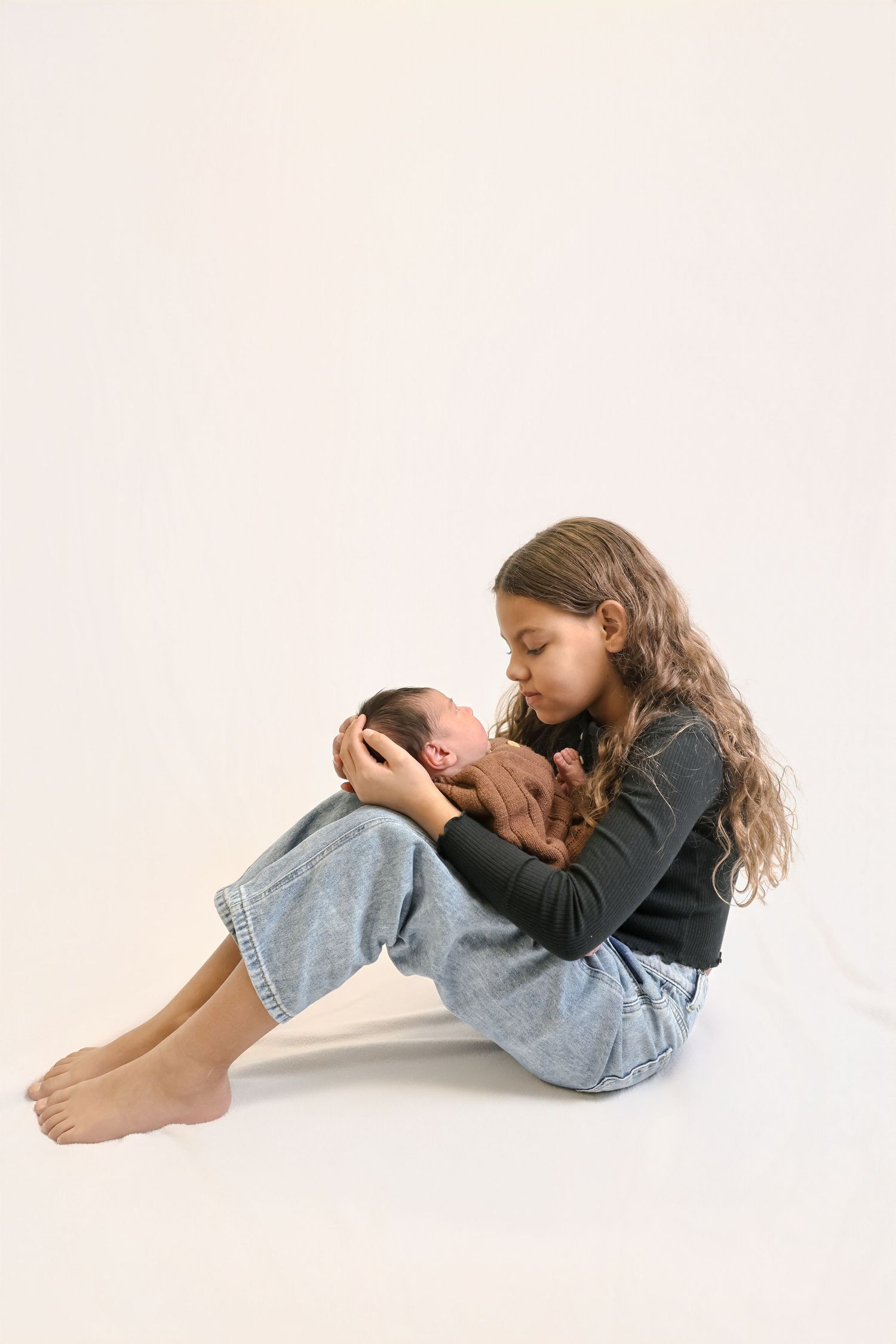 Young person in jeans and dark top lying curled up on white background in three progressive poses.