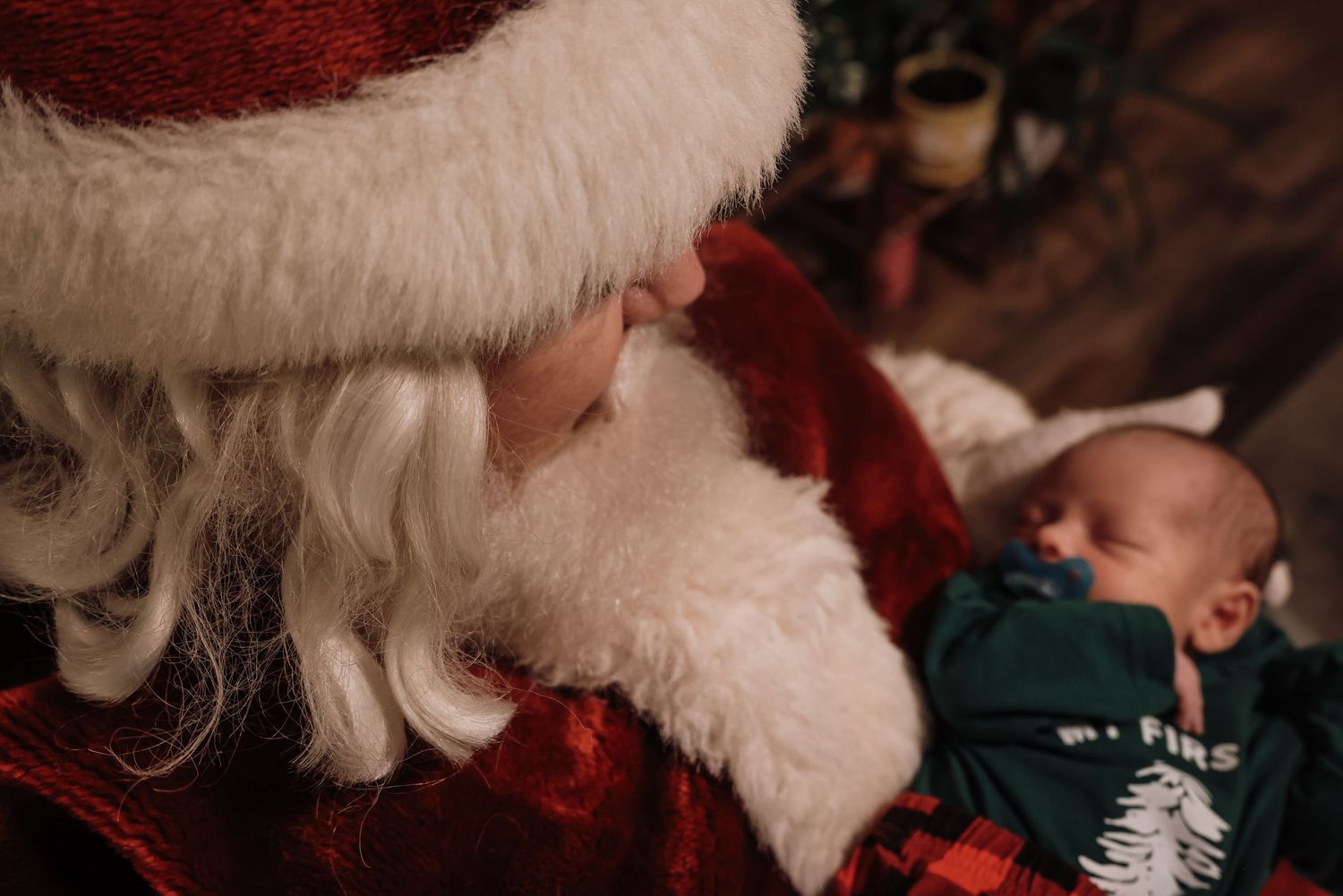 A sleeping baby in a green holiday sweater being watched over by Santa Claus with his white beard and red suit.
