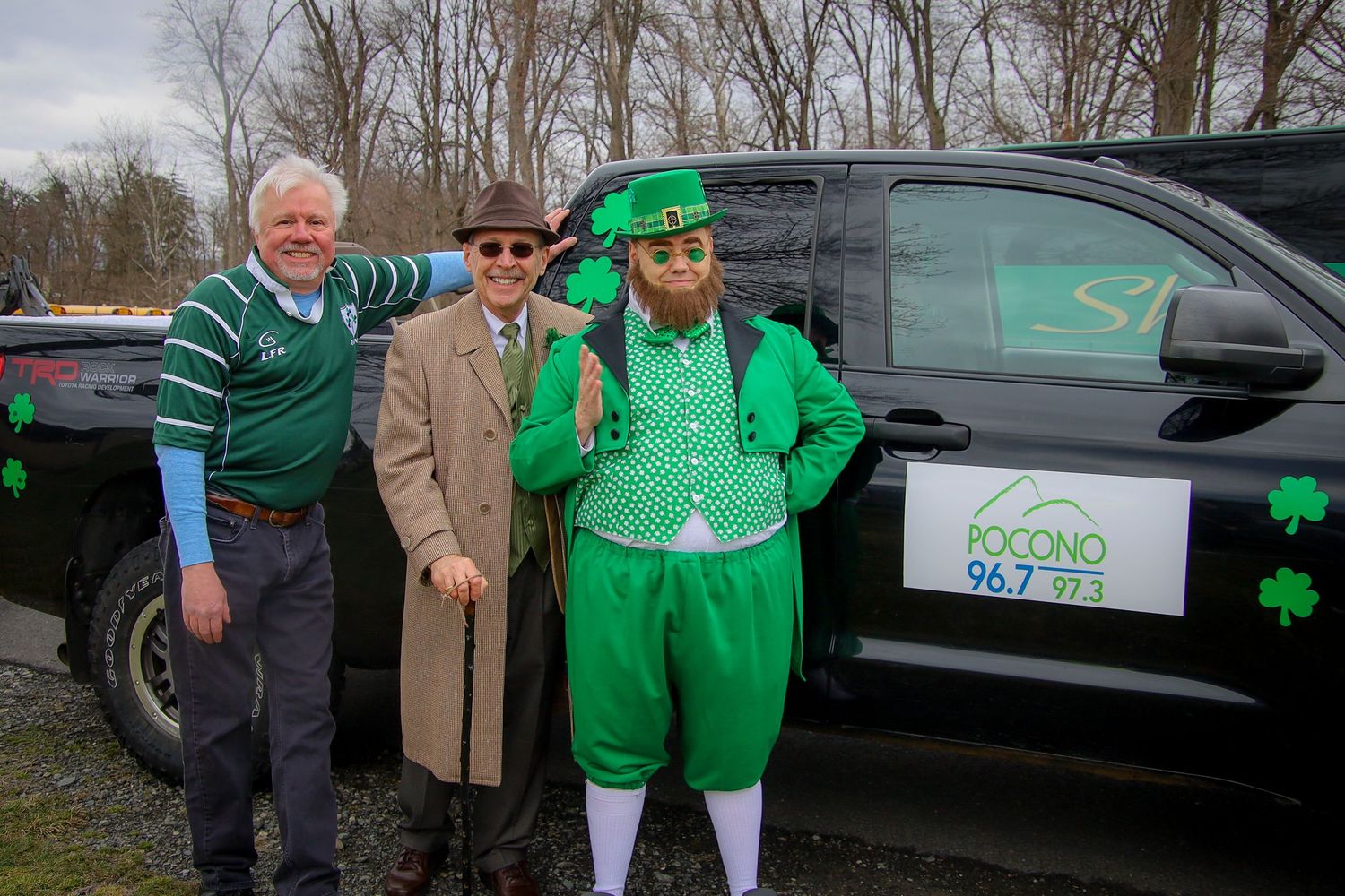 A group wearing green attire stands together near vehicles during what appears to be a community event.