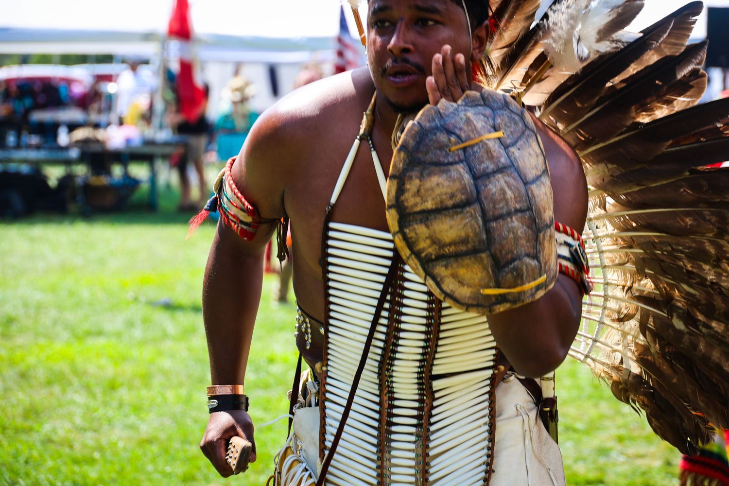 Native American dancers in traditional regalia perform at an outdoor powwow celebration on a grassy field.