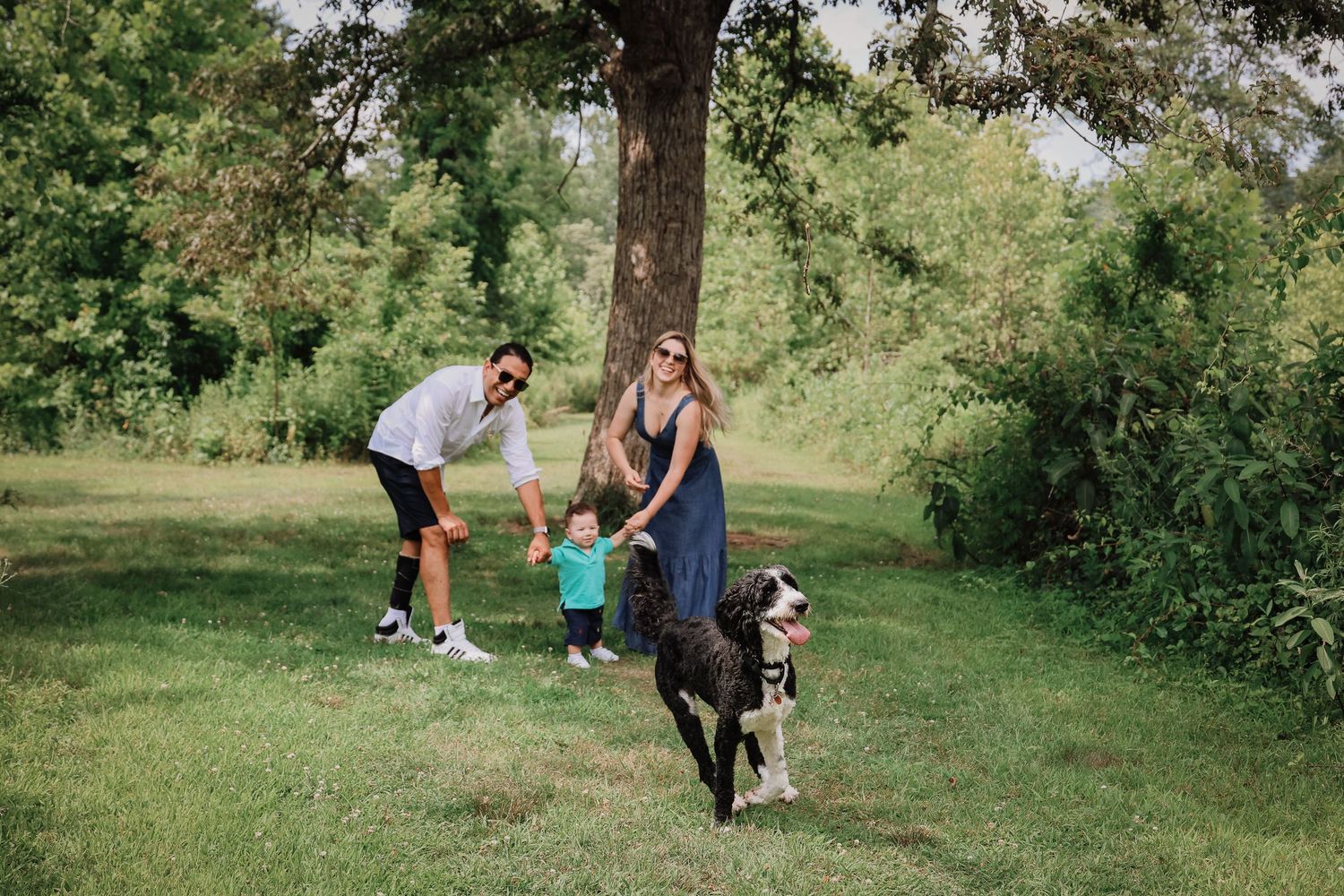 A couple poses for engagement photos in a lush green park setting during a summer photoshoot session.